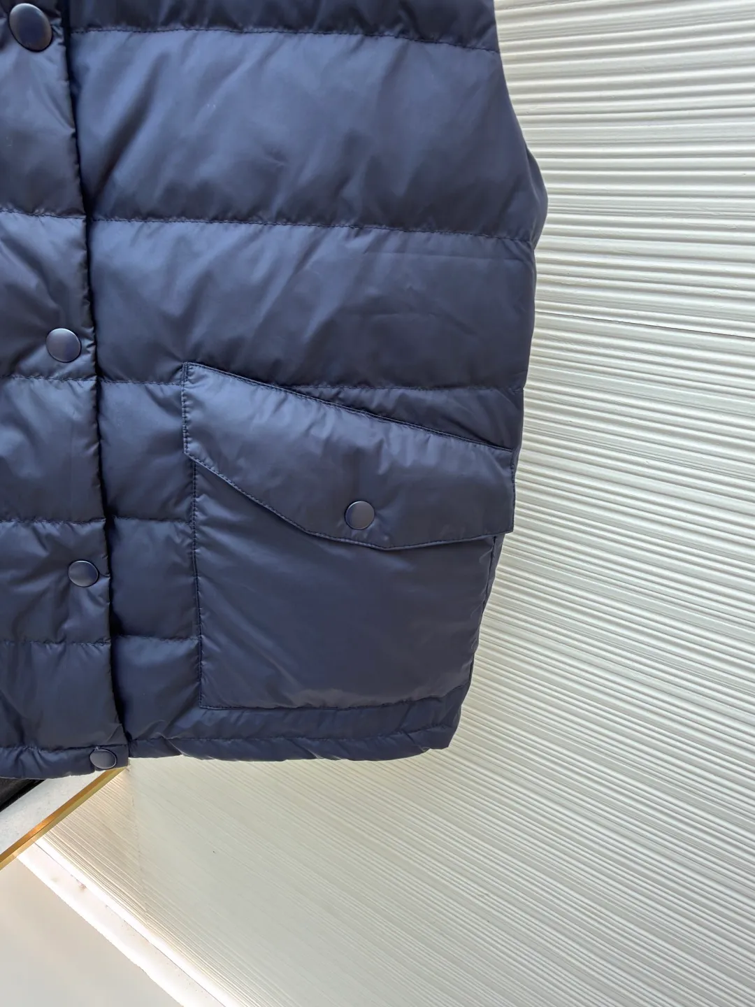 MIUMIU rib down lapel vest ●Original version: Purchased and developed for 12999 ●Item number: 1681785-C05 ●Fabric: goose down fabric ●Technology: mechanical down filling ●Color: navy blue ●Version: fitted version ●Weight: about 350 grams ●Size: 36-38-40-42 ●Description: Down anti-drilling liner is a kind of inner liner specially used for down jackets. It is usually made of high-density, anti-drilling down and good breathability materials. It can effectively prevent down from drilling out while maintaining the warmth and breathability of down jackets. Goose down filling is a high-quality filling in down jackets. It is rich in down, and because goose down has a higher loft, it can lock in more air, making the down jacket warmer. Down is soft and delicate. It feels soft and comfortable when worn on the human body, without the foreign body feeling caused by other fillings. After aurora printing, the pattern containing special additives is heat-pressed and transferred to the fabric in the form of a film, and the process parameters are adjusted to give it a slightly aged texture. This not only achieves the decorative purpose of the brand logo, but also avoids the stiffness often found in new technology fabrics because of its retro treatment of details. The design of the shirt collar allows the vest to increase its versatility. The snap closure provides a faster, smoother and more even force-on and take-off experience, especially when worn as an inner layer, making it less likely to snag with outer clothing. The elastic drawstring hem can be tightened by the drawstring, effectively preventing cold air from pouring in from the bottom and locking in body heat. The flap pocket is a classic outdoor functional design that prevents rain, wind and snow from entering the pocket, and is equipped with buttons for a more durable and quieter closure.