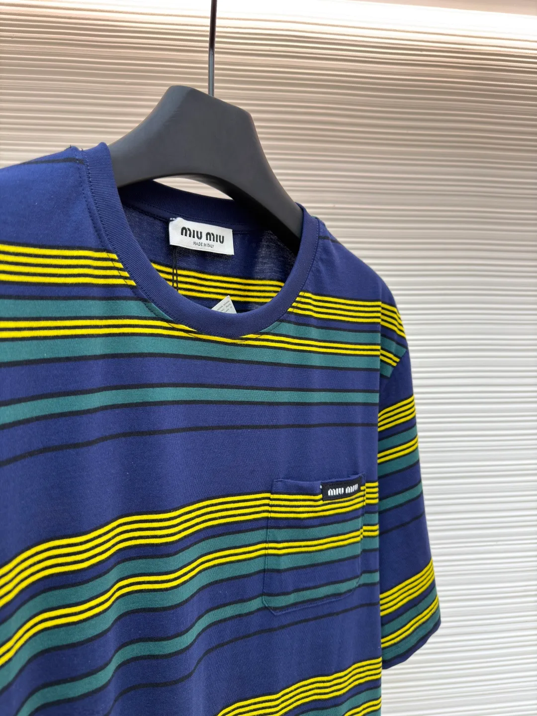 MIUMIU yellow, green and blue striped round neck short sleeves ●Original version: purchased and developed by 4755 ●Item number: 1681739-A10 ●Fabric: Jacquard striped knitted fabric ●Technology: Wool jacquard production ●Color: yellow, green and blue ●Version: Fitted version ●Weight: about 185 grams ●Size: XS-S-M-L ●Description: Using 32S jacquard stripe technology special textile compact cotton , 145g; with 32S double yarn frame, 380g. The fabric is made of 32-count combed cotton yarn and has been processed by compact spinning technology, so that the yarn fibers are tightly arranged and impurities and hairiness are significantly reduced. The fabric structure is denser and smoother. It not only feels delicate and smooth, but its wear resistance and anti-pilling performance is also far superior to ordinary cotton fabrics. The weight of the fabric ensures that the fabric has good durability while maintaining the natural breathability and skin-friendly properties of cotton. It is very suitable for spring, summer and transitional seasons, and achieves the unity of comfort and quality. The striped effect is achieved through plain knitting technology where colored yarns are alternately woven. This is different from later printing. The color is firm and long-lasting, and the striped edges are clear and neat. The design that combines simple stripes with the possible jacquard texture of the underlying fabric increases the visual layering, avoids monotony, and embodies the design idea of ​​finding sophistication in simplicity. The wool jacquard logo process is a high-end technology that weaves the brand logo directly into the fabric. The warp and weft yarns of the loom are controlled by computer programming, and yarns of different colors are interwoven to form precise and clear patterns on the surface of the sweater. The jacquard process makes the logo and logo fabric seamlessly integrated, with a smooth touch and no bulges, and clear and seamless edges, which greatly improves wearing comfort and aesthetics. The overall wiring is straight and delicate, the fabric is comfortable and soft, and the color is consistent without color difference. It can be matched with the same style to create a fashionable look and control various occasions. Customized accessories, complete with three standards, same style for men and women!