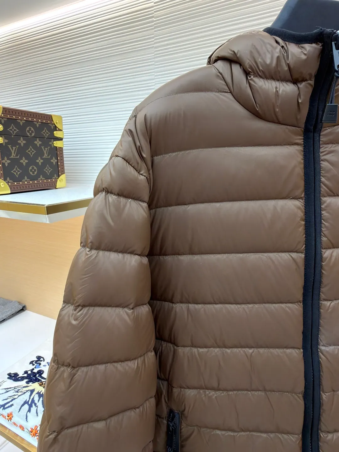 MIU MIU hooded down jacket ●Item number: 1681315-C55 ●Material: white duck down fabric ●Technology: mechanical down filling ●Color: brown ●Version: fitted version ●Weight: about 615 grams ●Size: S-M-L-XL ●Description: This is a light down jacket from the MiuMiu brand. Its craftsmanship details are as follows: It is made of exquisite pongé fabric made of 100% recycled polyester fiber. This fabric has good windproof performance, and at the same time has a delicate texture and a high-end luster. It has high fluffiness, excellent warmth retention and is very light overall, allowing the wearer to gain warmth without any heavy burden. It has a three-dimensional cut and a neat silhouette. Precision stitching technology is used during sewing to form regular quilting lines, which not only serves to fix the down, but also enhances the structure and design of the garment. The stitches are fine and even, and the seams are smooth, reflecting the exquisite craftsmanship of garment making. Equipped with a customized wax zipper, the zipper is smooth and durable, and the zipper puller has brand details and a high-quality feel. The hooded design fits the head and increases warmth; the drawstring cuffs can be adjusted according to needs to prevent cold wind from entering; the elastic drawstring at the hem can adjust the looseness of the hem, improving the comfort and practicality of wearing; there is the brand's embroidered logo on the chest, with fine craftsmanship and highlighting the brand identity.