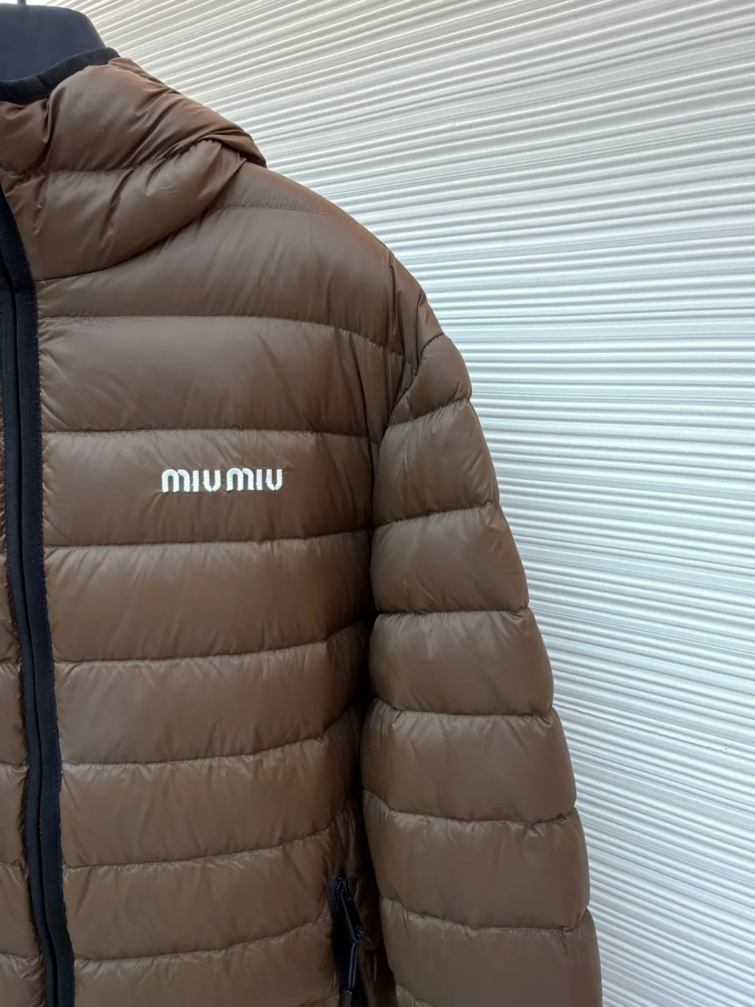 MIU MIU hooded down jacket ●Item number: 1681315-C55 ●Material: white duck down fabric ●Technology: mechanical down filling ●Color: brown ●Version: fitted version ●Weight: about 615 grams ●Size: S-M-L-XL ●Description: This is a light down jacket from the MiuMiu brand. Its craftsmanship details are as follows: It is made of exquisite pongé fabric made of 100% recycled polyester fiber. This fabric has good windproof performance, and at the same time has a delicate texture and a high-end luster. It has high fluffiness, excellent warmth retention and is very light overall, allowing the wearer to gain warmth without any heavy burden. It has a three-dimensional cut and a neat silhouette. Precision stitching technology is used during sewing to form regular quilting lines, which not only serves to fix the down, but also enhances the structure and design of the garment. The stitches are fine and even, and the seams are smooth, reflecting the exquisite craftsmanship of garment making. Equipped with a customized wax zipper, the zipper is smooth and durable, and the zipper puller has brand details and a high-quality feel. The hooded design fits the head and increases warmth; the drawstring cuffs can be adjusted according to needs to prevent cold wind from entering; the elastic drawstring at the hem can adjust the looseness of the hem, improving the comfort and practicality of wearing; there is the brand's embroidered logo on the chest, with fine craftsmanship and highlighting the brand identity.