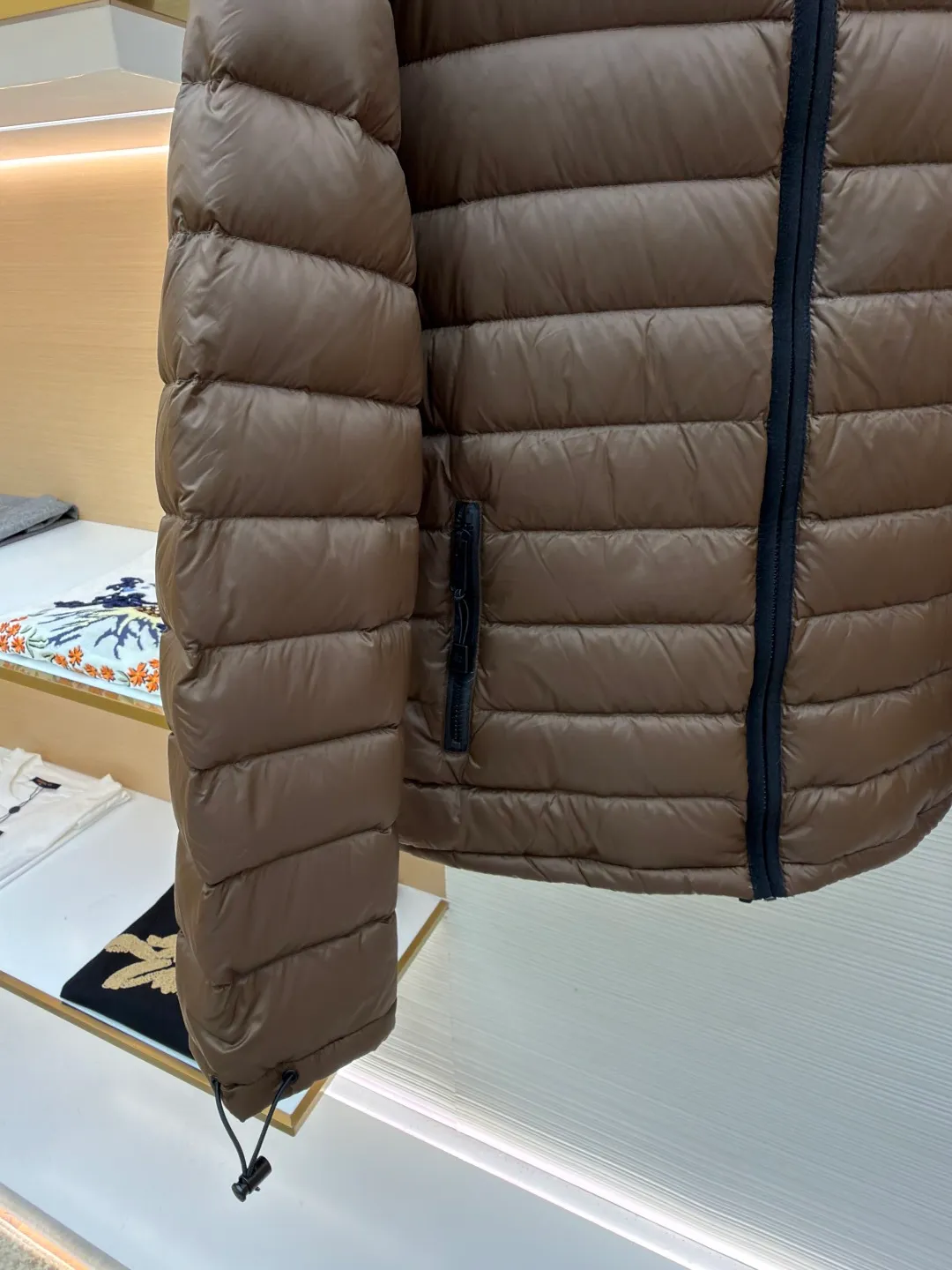 MIU MIU hooded down jacket ●Item number: 1681315-C55 ●Material: white duck down fabric ●Technology: mechanical down filling ●Color: brown ●Version: fitted version ●Weight: about 615 grams ●Size: S-M-L-XL ●Description: This is a light down jacket from the MiuMiu brand. Its craftsmanship details are as follows: It is made of exquisite pongé fabric made of 100% recycled polyester fiber. This fabric has good windproof performance, and at the same time has a delicate texture and a high-end luster. It has high fluffiness, excellent warmth retention and is very light overall, allowing the wearer to gain warmth without any heavy burden. It has a three-dimensional cut and a neat silhouette. Precision stitching technology is used during sewing to form regular quilting lines, which not only serves to fix the down, but also enhances the structure and design of the garment. The stitches are fine and even, and the seams are smooth, reflecting the exquisite craftsmanship of garment making. Equipped with a customized wax zipper, the zipper is smooth and durable, and the zipper puller has brand details and a high-quality feel. The hooded design fits the head and increases warmth; the drawstring cuffs can be adjusted according to needs to prevent cold wind from entering; the elastic drawstring at the hem can adjust the looseness of the hem, improving the comfort and practicality of wearing; there is the brand's embroidered logo on the chest, with fine craftsmanship and highlighting the brand identity.