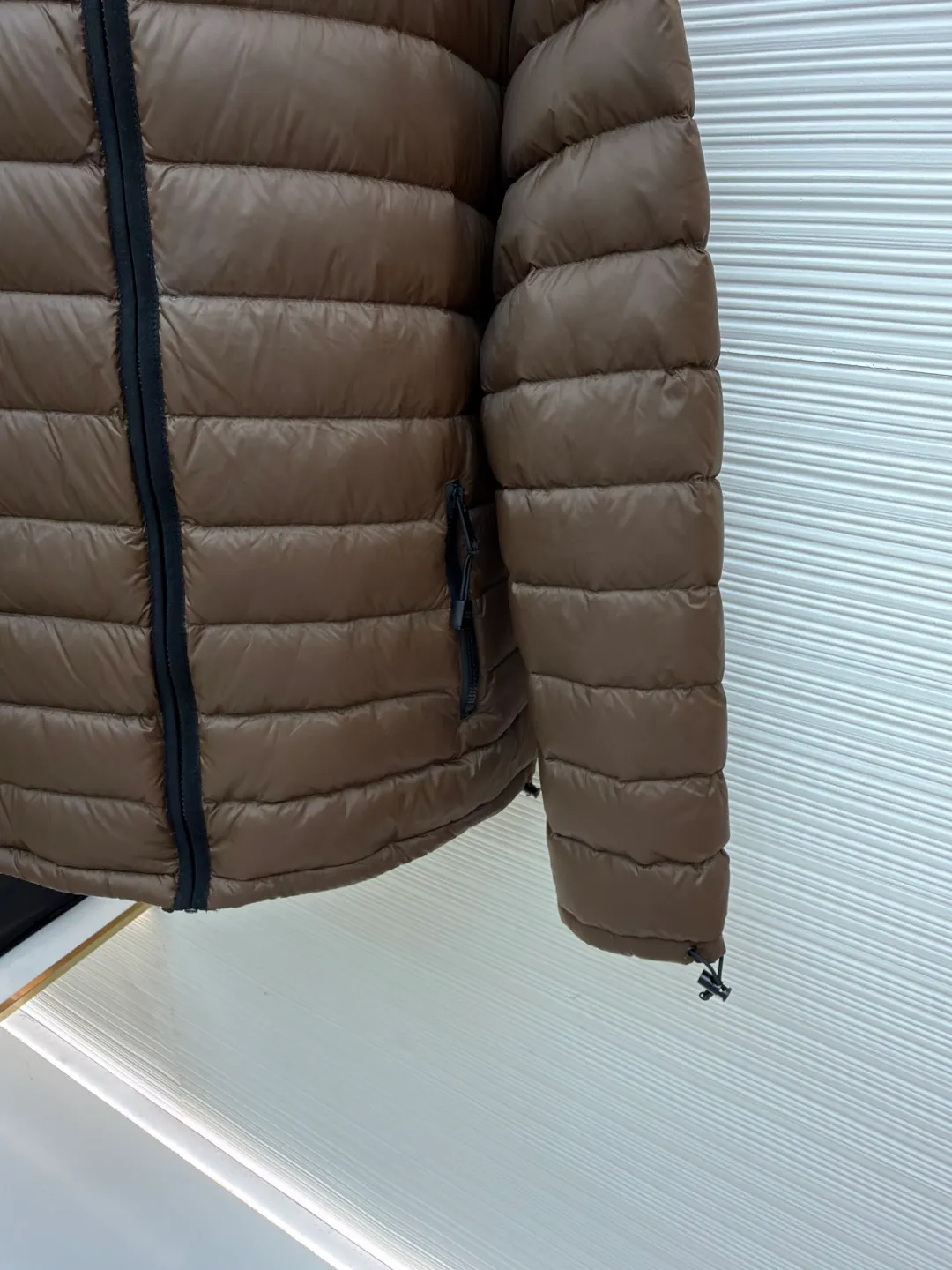 MIU MIU hooded down jacket ●Item number: 1681315-C55 ●Material: white duck down fabric ●Technology: mechanical down filling ●Color: brown ●Version: fitted version ●Weight: about 615 grams ●Size: S-M-L-XL ●Description: This is a light down jacket from the MiuMiu brand. Its craftsmanship details are as follows: It is made of exquisite pongé fabric made of 100% recycled polyester fiber. This fabric has good windproof performance, and at the same time has a delicate texture and a high-end luster. It has high fluffiness, excellent warmth retention and is very light overall, allowing the wearer to gain warmth without any heavy burden. It has a three-dimensional cut and a neat silhouette. Precision stitching technology is used during sewing to form regular quilting lines, which not only serves to fix the down, but also enhances the structure and design of the garment. The stitches are fine and even, and the seams are smooth, reflecting the exquisite craftsmanship of garment making. Equipped with a customized wax zipper, the zipper is smooth and durable, and the zipper puller has brand details and a high-quality feel. The hooded design fits the head and increases warmth; the drawstring cuffs can be adjusted according to needs to prevent cold wind from entering; the elastic drawstring at the hem can adjust the looseness of the hem, improving the comfort and practicality of wearing; there is the brand's embroidered logo on the chest, with fine craftsmanship and highlighting the brand identity.