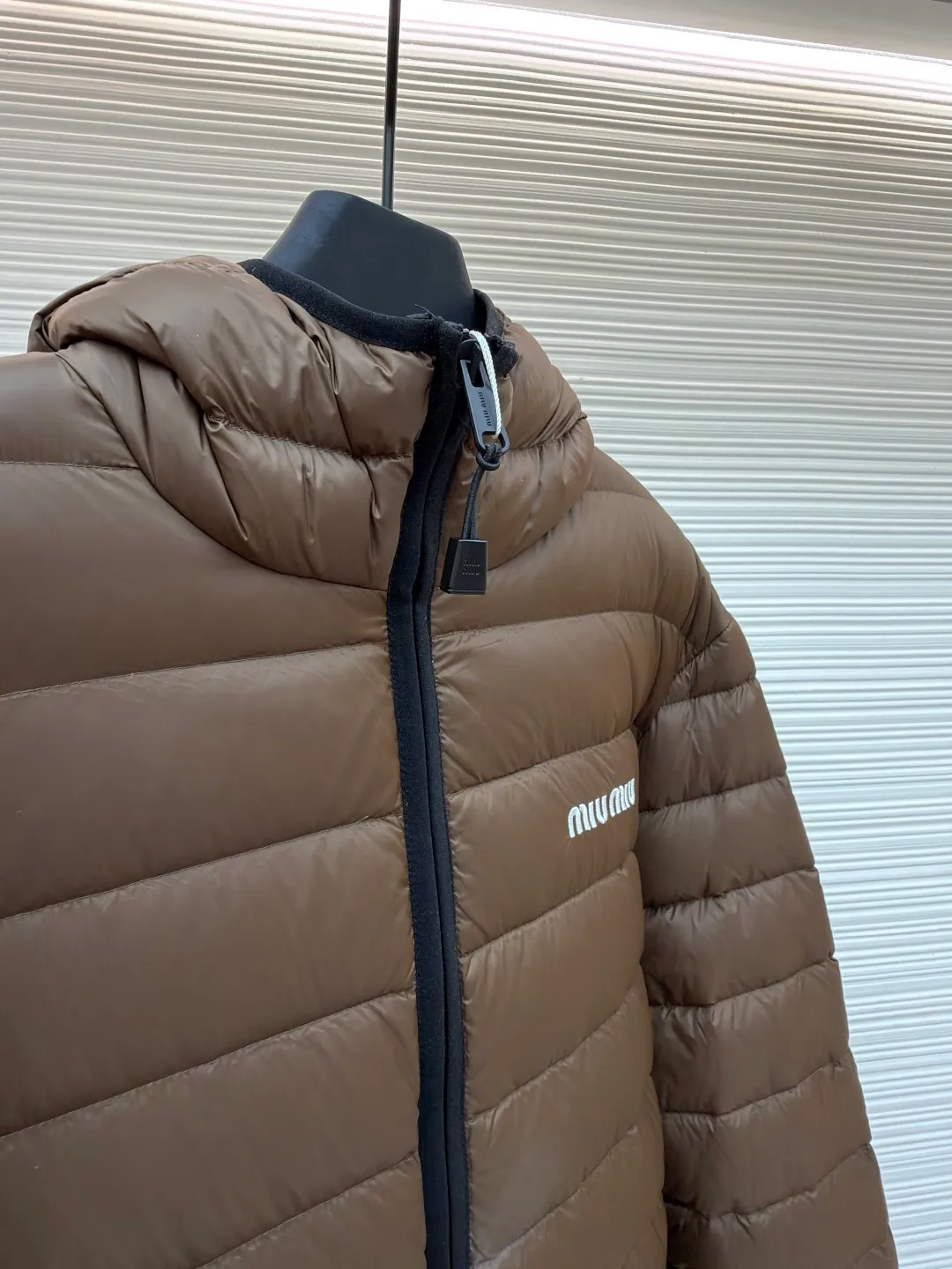 MIU MIU hooded down jacket ●Item number: 1681315-C55 ●Material: white duck down fabric ●Technology: mechanical down filling ●Color: brown ●Version: fitted version ●Weight: about 615 grams ●Size: S-M-L-XL ●Description: This is a light down jacket from the MiuMiu brand. Its craftsmanship details are as follows: It is made of exquisite pongé fabric made of 100% recycled polyester fiber. This fabric has good windproof performance, and at the same time has a delicate texture and a high-end luster. It has high fluffiness, excellent warmth retention and is very light overall, allowing the wearer to gain warmth without any heavy burden. It has a three-dimensional cut and a neat silhouette. Precision stitching technology is used during sewing to form regular quilting lines, which not only serves to fix the down, but also enhances the structure and design of the garment. The stitches are fine and even, and the seams are smooth, reflecting the exquisite craftsmanship of garment making. Equipped with a customized wax zipper, the zipper is smooth and durable, and the zipper puller has brand details and a high-quality feel. The hooded design fits the head and increases warmth; the drawstring cuffs can be adjusted according to needs to prevent cold wind from entering; the elastic drawstring at the hem can adjust the looseness of the hem, improving the comfort and practicality of wearing; there is the brand's embroidered logo on the chest, with fine craftsmanship and highlighting the brand identity.