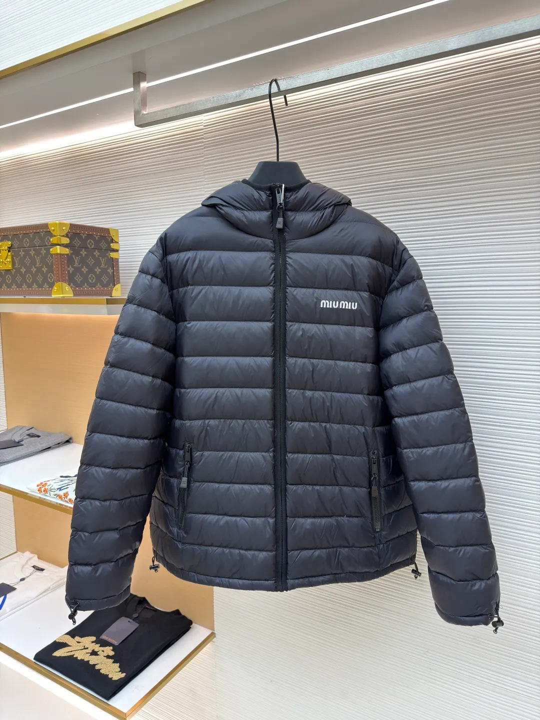 MIU MIU hooded down jacket ●Item number: 1681314-C55 ●Material: white duck down fabric ●Technology: mechanical down filling ●Color: black ●Version: fitted version ●Weight: about 615 grams ●Size: S-M-L-XL ●Description: This is a light down jacket from the MiuMiu brand. Its craftsmanship details are as follows: It is made of exquisite pongé fabric made of 100% recycled polyester fiber. This fabric has good windproof performance, and at the same time has a delicate texture and a high-end luster. It has high fluffiness, excellent warmth retention and is very light overall, allowing the wearer to gain warmth without any heavy burden. It has a three-dimensional cut and a neat silhouette. Precision stitching technology is used during sewing to form regular quilting lines, which not only serves to fix the down, but also enhances the structure and design of the garment. The stitches are fine and even, and the seams are smooth, reflecting the exquisite craftsmanship of garment making. Equipped with a customized wax zipper, the zipper is smooth and durable, and the zipper puller has brand details and a high-quality feel. The hooded design fits the head and increases warmth; the drawstring cuffs can be adjusted according to needs to prevent cold wind from entering; the elastic drawstring at the hem can adjust the looseness of the hem, improving the comfort and practicality of wearing; there is the brand's embroidered logo on the chest, with fine craftsmanship and highlighting the brand identity.
