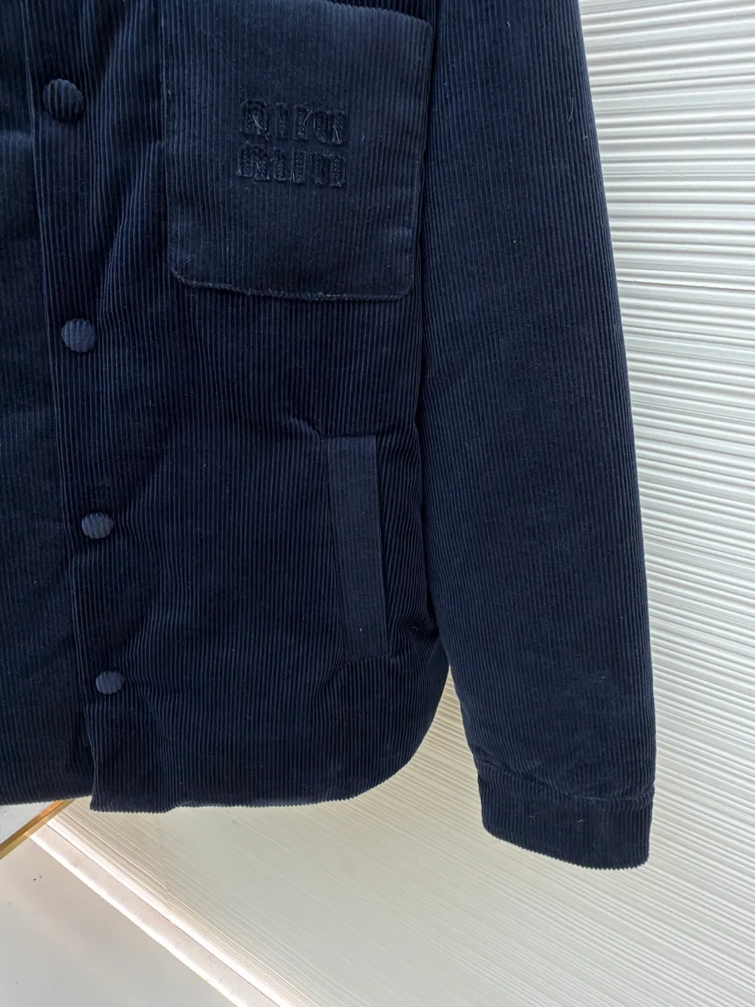 MIUMIU leather collar corduroy down jacket ●Original version: purchased and developed by 16097 ●Item number: 1681743-C75 ●Fabric: corduroy fabric ●Technology: patch embroidery production ●Color: navy blue ●Version: fitted version ●Weight: about 935 grams ●Size: 46-48-50-52 ●Description: When embroidery of the same color quietly grows among the corduroy textures - MIUMIU redefines winter elegance with "hidden beauty", making warmth a tacit whisper. Classic fine-ribbed corduroy wraps the body, with down like clouds lurking between the convex and convex warps and wefts. 90% white duck down silently resists the cold wind, but lets the fabric speak for itself - every velvet is the path of sunlight, and every ridge is a fortress built by warmth. The custom-made lambskin lapel falls along the curve of the neck, making it breathable like a second skin. Cold leather and soft suede complete a material game on the collar, and the sound of metal snaps opening and closing becomes the only punctuation mark in this dialogue. Exquisite appliqué technology performs visual magic on the left breast pocket: the embroidered letter patches are laser cut and shaped to create an embossed texture and clear fonts. Each patch undergoes 5 layers of anti-wrinkle treatment to ensure that it retains its original shape after washing. The embroidered fabric of the same color as the fabric runs along the MIUMIU logo, with only subtle gloss differences and raised stitches to enhance visual recognition. The overall wiring is straight and delicate, the fabric is comfortable and soft, and the color is consistent without color difference. It can be matched with the same style to create a fashionable look and control various occasions. Customized accessories, complete with three standards, same style for men and women!