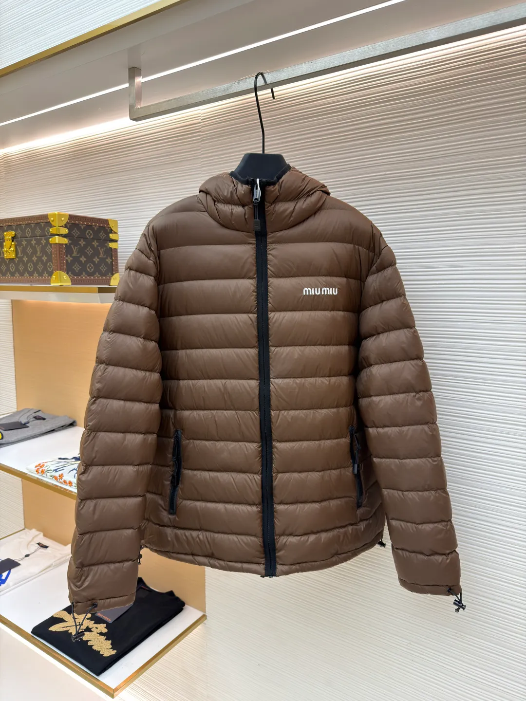 MIU MIU hooded down jacket ●Item number: 1681315-C55 ●Material: white duck down fabric ●Technology: mechanical down filling ●Color: brown ●Version: fitted version ●Weight: about 615 grams ●Size: S-M-L-XL ●Description: This is a light down jacket from the MiuMiu brand. Its craftsmanship details are as follows: It is made of exquisite pongé fabric made of 100% recycled polyester fiber. This fabric has good windproof performance, and at the same time has a delicate texture and a high-end luster. It has high fluffiness, excellent warmth retention and is very light overall, allowing the wearer to gain warmth without any heavy burden. It has a three-dimensional cut and a neat silhouette. Precision stitching technology is used during sewing to form regular quilting lines, which not only serves to fix the down, but also enhances the structure and design of the garment. The stitches are fine and even, and the seams are smooth, reflecting the exquisite craftsmanship of garment making. Equipped with a customized wax zipper, the zipper is smooth and durable, and the zipper puller has brand details and a high-quality feel. The hooded design fits the head and increases warmth; the drawstring cuffs can be adjusted according to needs to prevent cold wind from entering; the elastic drawstring at the hem can adjust the looseness of the hem, improving the comfort and practicality of wearing; there is the brand's embroidered logo on the chest, with fine craftsmanship and highlighting the brand identity.