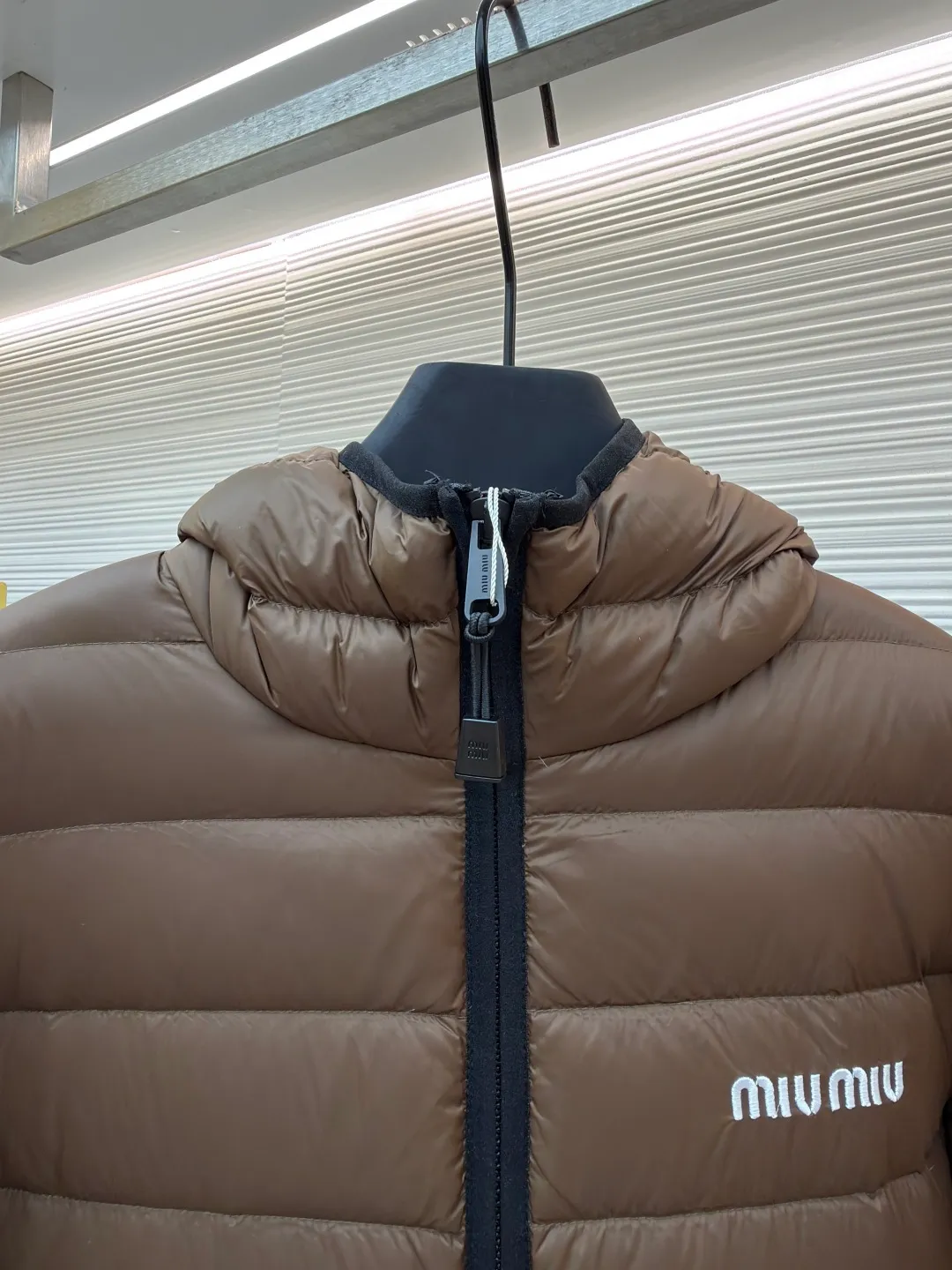 MIU MIU hooded down jacket ●Item number: 1681315-C55 ●Material: white duck down fabric ●Technology: mechanical down filling ●Color: brown ●Version: fitted version ●Weight: about 615 grams ●Size: S-M-L-XL ●Description: This is a light down jacket from the MiuMiu brand. Its craftsmanship details are as follows: It is made of exquisite pongé fabric made of 100% recycled polyester fiber. This fabric has good windproof performance, and at the same time has a delicate texture and a high-end luster. It has high fluffiness, excellent warmth retention and is very light overall, allowing the wearer to gain warmth without any heavy burden. It has a three-dimensional cut and a neat silhouette. Precision stitching technology is used during sewing to form regular quilting lines, which not only serves to fix the down, but also enhances the structure and design of the garment. The stitches are fine and even, and the seams are smooth, reflecting the exquisite craftsmanship of garment making. Equipped with a customized wax zipper, the zipper is smooth and durable, and the zipper puller has brand details and a high-quality feel. The hooded design fits the head and increases warmth; the drawstring cuffs can be adjusted according to needs to prevent cold wind from entering; the elastic drawstring at the hem can adjust the looseness of the hem, improving the comfort and practicality of wearing; there is the brand's embroidered logo on the chest, with fine craftsmanship and highlighting the brand identity.