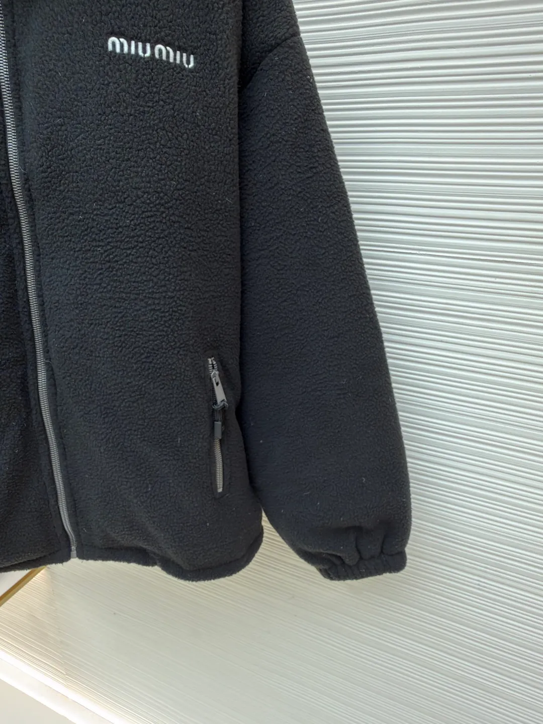 MIUMIU Polar Fleece Collar Down Jacket ●Original version: purchased and developed at 16999 ●Item number: 1681395-C65 ●Fabric: polar fleece fabric ●Technology: made on positioning cutting machine ●Color: black ●Version: fitted version ●Weight: about 945 grams ●Size: 38-40-42-44 ●Description: This jacket is made of high-quality polar fleece fabric and treated with a special fleece process. It feels soft and fluffy and has excellent warmth retention. The collar is made of imitation lambswool and is made through flocking technology, forming a texture contrast with the polar fleece fabric. The main zipper is a custom-made metal zipper, which is smooth and durable; the zippers of the zipper pockets on both sides are made of the same material as the main zipper, combining practicality and design. The brand logo adopts exquisite embroidery technology, and the stitching is fine and firm. The drawstring at the hem adopts a metal buckle and can be adjusted for tightness. The overall sewing adopts flat seam technology, the stitch spacing is even, and the seams of the body are smooth and snug. From the comfortable texture of the fabric to the craftsmanship of the details, it reflects the brand's dual pursuit of fashion and quality. It is a single product with both warmth and design. The overall wiring is straight and delicate, the fabric is comfortable and soft, and the color is consistent without color difference. It can be matched with the same style to create a fashionable look and control various occasions. Customized accessories, complete with three standards, same style for men and women!