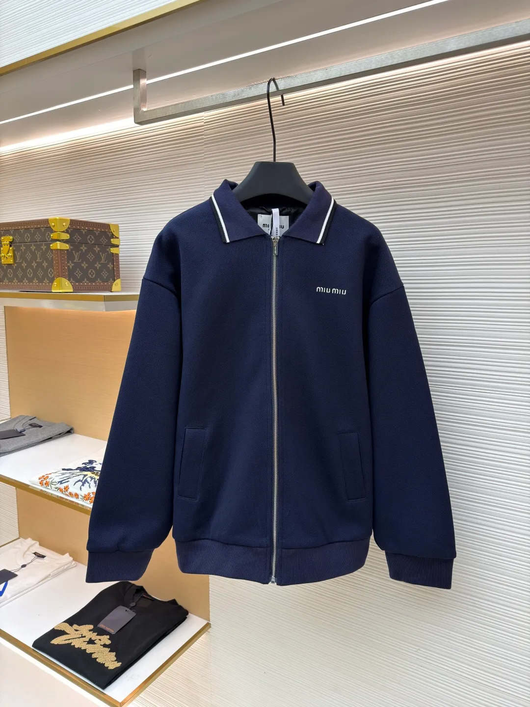 MIUMIU letter embroidered pique lapel jacket ●Original version: 25400 purchased and developed ●Item number: 1681338-B20 ●Material: combed cotton fabric ●Technology: embroidery production ●Color: navy ●Version: Fitted version ●Weight: about 1130 grams ●Size: 36-38-40-42 ●Description: This jacket is made of high-count combed cotton blended fabric, which is crisp and soft to the touch. The neckline is a classic lapel design, and the edges are decorated with double topstitching in contrasting colors. The black and white lines are precisely aligned, demonstrating the brand's control of details. The placket is equipped with a custom metal zipper. Its smoothness has been tested many times for wear resistance, and there is no lag when closing. The "miu miu" logo on the chest adopts high-precision embroidery technology, with fine and even stitching and full three-dimensionality. There are three-dimensional pockets on both sides of the body, and the edges of the pockets are hemmed to prevent the fabric from coming off. The ribs on the cuffs and hem are made of high-elastic knitting technology to ensure fit and resilience when worn. The overall tailoring follows an oversize silhouette, and the splicing of the body uses double stitching + overlocking techniques to ensure fastness and prevent threads from being exposed. Every craft detail reflects the brand's high-end clothing making standards.
