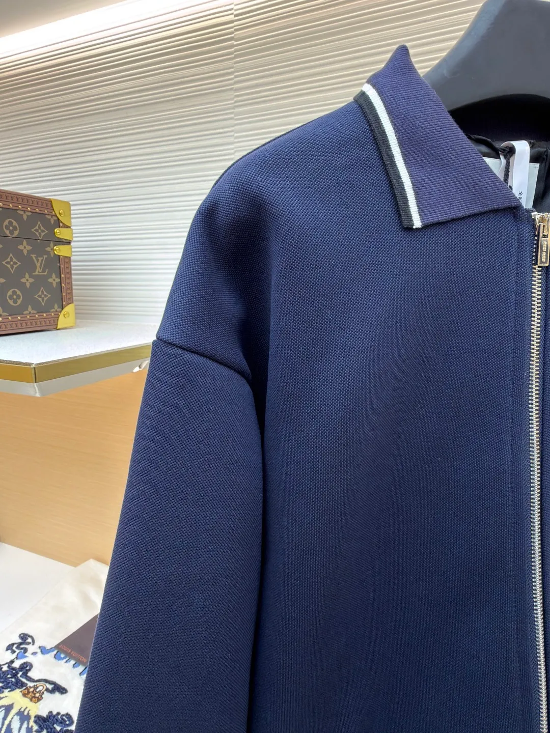 MIUMIU letter embroidered pique lapel jacket ●Original version: 25400 purchased and developed ●Item number: 1681338-B20 ●Material: combed cotton fabric ●Technology: embroidery production ●Color: navy ●Version: Fitted version ●Weight: about 1130 grams ●Size: 36-38-40-42 ●Description: This jacket is made of high-count combed cotton blended fabric, which is crisp and soft to the touch. The neckline is a classic lapel design, and the edges are decorated with double topstitching in contrasting colors. The black and white lines are precisely aligned, demonstrating the brand's control of details. The placket is equipped with a custom metal zipper. Its smoothness has been tested many times for wear resistance, and there is no lag when closing. The "miu miu" logo on the chest adopts high-precision embroidery technology, with fine and even stitching and full three-dimensionality. There are three-dimensional pockets on both sides of the body, and the edges of the pockets are hemmed to prevent the fabric from coming off. The ribs on the cuffs and hem are made of high-elastic knitting technology to ensure fit and resilience when worn. The overall tailoring follows an oversize silhouette, and the splicing of the body uses double stitching + overlocking techniques to ensure fastness and prevent threads from being exposed. Every craft detail reflects the brand's high-end clothing making standards.