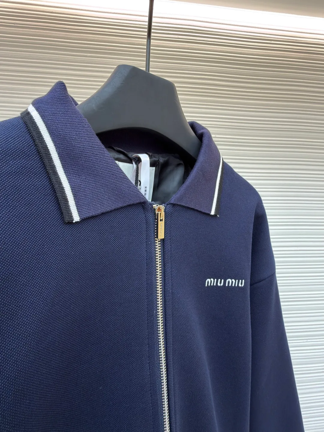 MIUMIU letter embroidered pique lapel jacket ●Original version: 25400 purchased and developed ●Item number: 1681338-B20 ●Material: combed cotton fabric ●Technology: embroidery production ●Color: navy ●Version: Fitted version ●Weight: about 1130 grams ●Size: 36-38-40-42 ●Description: This jacket is made of high-count combed cotton blended fabric, which is crisp and soft to the touch. The neckline is a classic lapel design, and the edges are decorated with double topstitching in contrasting colors. The black and white lines are precisely aligned, demonstrating the brand's control of details. The placket is equipped with a custom metal zipper. Its smoothness has been tested many times for wear resistance, and there is no lag when closing. The "miu miu" logo on the chest adopts high-precision embroidery technology, with fine and even stitching and full three-dimensionality. There are three-dimensional pockets on both sides of the body, and the edges of the pockets are hemmed to prevent the fabric from coming off. The ribs on the cuffs and hem are made of high-elastic knitting technology to ensure fit and resilience when worn. The overall tailoring follows an oversize silhouette, and the splicing of the body uses double stitching + overlocking techniques to ensure fastness and prevent threads from being exposed. Every craft detail reflects the brand's high-end clothing making standards.