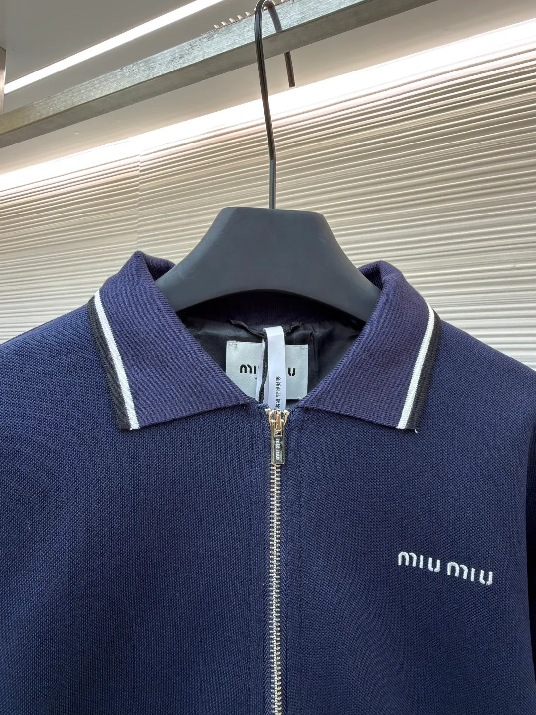 MIUMIU letter embroidered pique lapel jacket ●Original version: 25400 purchased and developed ●Item number: 1681338-B20 ●Material: combed cotton fabric ●Technology: embroidery production ●Color: navy ●Version: Fitted version ●Weight: about 1130 grams ●Size: 36-38-40-42 ●Description: This jacket is made of high-count combed cotton blended fabric, which is crisp and soft to the touch. The neckline is a classic lapel design, and the edges are decorated with double topstitching in contrasting colors. The black and white lines are precisely aligned, demonstrating the brand's control of details. The placket is equipped with a custom metal zipper. Its smoothness has been tested many times for wear resistance, and there is no lag when closing. The "miu miu" logo on the chest adopts high-precision embroidery technology, with fine and even stitching and full three-dimensionality. There are three-dimensional pockets on both sides of the body, and the edges of the pockets are hemmed to prevent the fabric from coming off. The ribs on the cuffs and hem are made of high-elastic knitting technology to ensure fit and resilience when worn. The overall tailoring follows an oversize silhouette, and the splicing of the body uses double stitching + overlocking techniques to ensure fastness and prevent threads from being exposed. Every craft detail reflects the brand's high-end clothing making standards.
