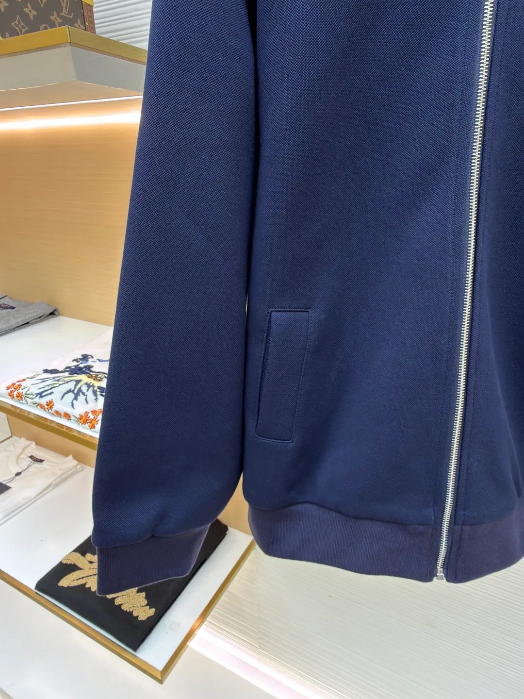 MIUMIU letter embroidered pique lapel jacket ●Original version: 25400 purchased and developed ●Item number: 1681338-B20 ●Material: combed cotton fabric ●Technology: embroidery production ●Color: navy ●Version: Fitted version ●Weight: about 1130 grams ●Size: 36-38-40-42 ●Description: This jacket is made of high-count combed cotton blended fabric, which is crisp and soft to the touch. The neckline is a classic lapel design, and the edges are decorated with double topstitching in contrasting colors. The black and white lines are precisely aligned, demonstrating the brand's control of details. The placket is equipped with a custom metal zipper. Its smoothness has been tested many times for wear resistance, and there is no lag when closing. The "miu miu" logo on the chest adopts high-precision embroidery technology, with fine and even stitching and full three-dimensionality. There are three-dimensional pockets on both sides of the body, and the edges of the pockets are hemmed to prevent the fabric from coming off. The ribs on the cuffs and hem are made of high-elastic knitting technology to ensure fit and resilience when worn. The overall tailoring follows an oversize silhouette, and the splicing of the body uses double stitching + overlocking techniques to ensure fastness and prevent threads from being exposed. Every craft detail reflects the brand's high-end clothing making standards.