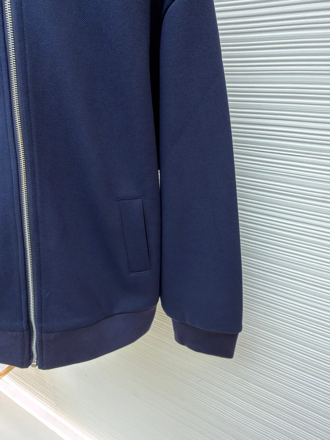 MIUMIU letter embroidered pique lapel jacket ●Original version: 25400 purchased and developed ●Item number: 1681338-B20 ●Material: combed cotton fabric ●Technology: embroidery production ●Color: navy ●Version: Fitted version ●Weight: about 1130 grams ●Size: 36-38-40-42 ●Description: This jacket is made of high-count combed cotton blended fabric, which is crisp and soft to the touch. The neckline is a classic lapel design, and the edges are decorated with double topstitching in contrasting colors. The black and white lines are precisely aligned, demonstrating the brand's control of details. The placket is equipped with a custom metal zipper. Its smoothness has been tested many times for wear resistance, and there is no lag when closing. The "miu miu" logo on the chest adopts high-precision embroidery technology, with fine and even stitching and full three-dimensionality. There are three-dimensional pockets on both sides of the body, and the edges of the pockets are hemmed to prevent the fabric from coming off. The ribs on the cuffs and hem are made of high-elastic knitting technology to ensure fit and resilience when worn. The overall tailoring follows an oversize silhouette, and the splicing of the body uses double stitching + overlocking techniques to ensure fastness and prevent threads from being exposed. Every craft detail reflects the brand's high-end clothing making standards.