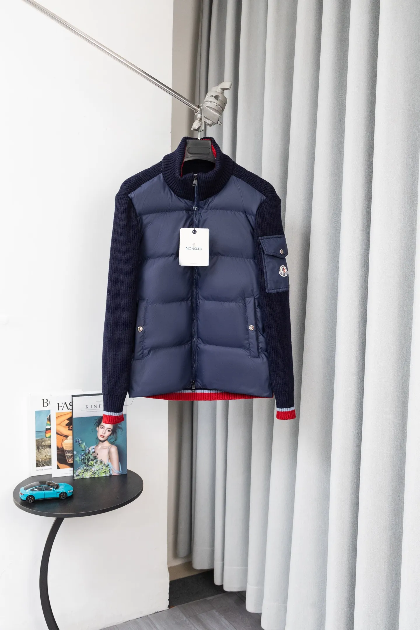 P560 Style number: M046 This is a knitted patchwork down jacket from Moncler. It combines the brand's high-end outdoor genes and fashion design. It is a luxurious item with both warmth and style in autumn and winter. Design highlights: Material splicing: Pure wool knitted sleeves are spliced ​​with a down front filled with 90 white duck down. The knitted part is soft and breathable, and the down part is fluffy and warm, achieving a dual fusion of style and function.  Detailed logo: The iconic Moncler badge pocket on the left arm is a classic embodiment of brand recognition; the stand-up collar design with a two-way zipper not only improves warmth, but also strengthens the neat styling.  Color embellishment: The contrasting red and blue stripes on the cuffs and hem inject vitality into the overall black tone, adding a retro college style charm. Craftsmanship and Quality: The down filling follows the European standard 90 down standard, with excellent fluffiness and down filling, with almost no stiff feeling. At the same time, it adopts the "line first and then separate down filling" process. The four-layer liner effectively prevents down from being drilled, and can maintain warmth even after long-term wear.  The knitted part is made of high-quality wool, which has a delicate touch and is not easily deformed. The splicing process with the down fabric is rigorous, showing a high-end texture level.  Style and Wearing This down jacket is based on the classic college style. The slim straight version can modify the body line and can be easily adapted to a variety of styles: it can be paired with jeans and casual shoes for a casual look on a daily basis. It can also be upgraded to an urban light luxury style by layering it with a turtleneck sweater inside and a suit outside. It is a key item in the winter wardrobe that is both practical and fashionable. Color: black, navy blue, sizes S-XL
