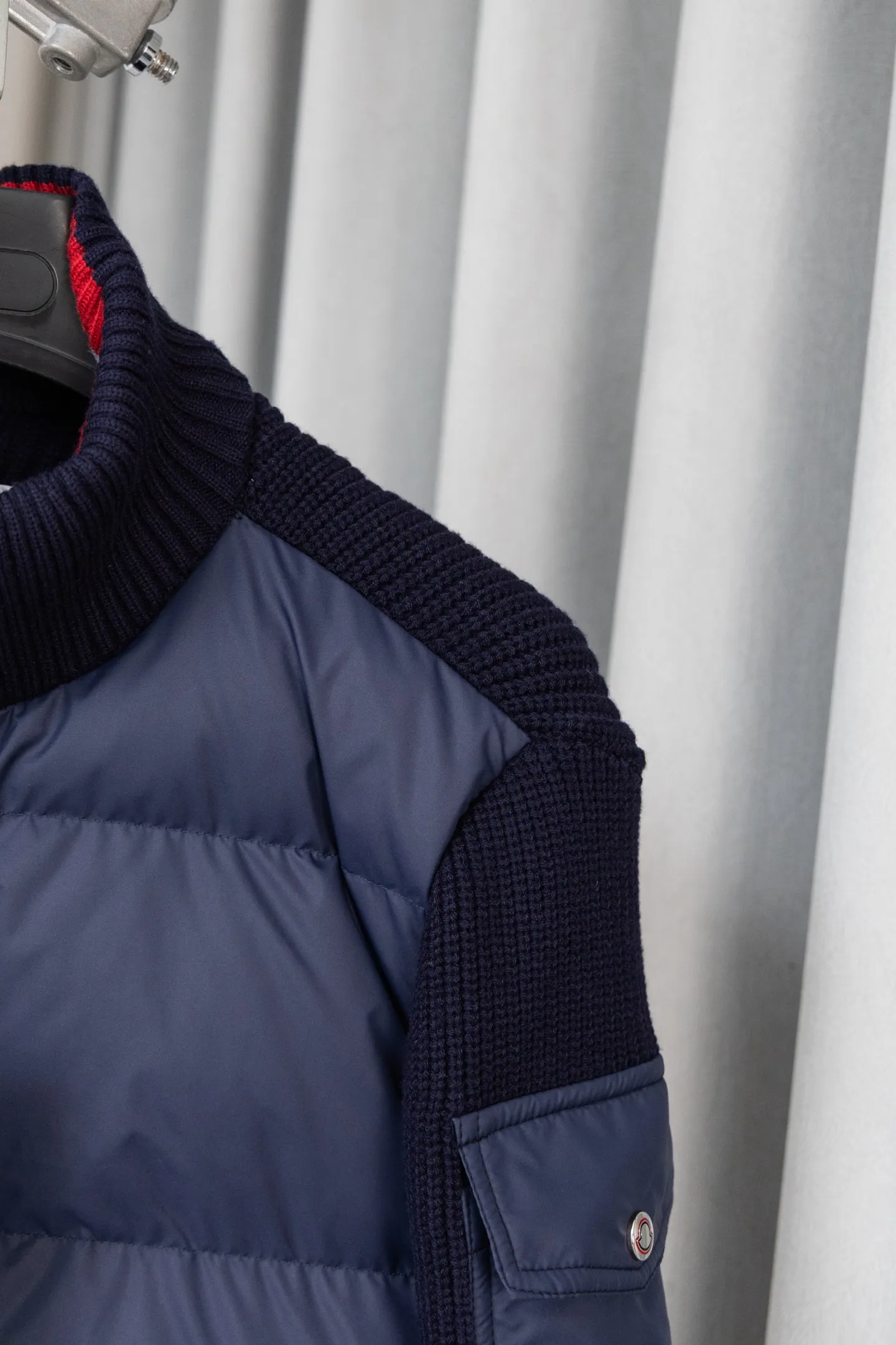 P560 Style number: M046 This is a knitted patchwork down jacket from Moncler. It combines the brand's high-end outdoor genes and fashion design. It is a luxurious item with both warmth and style in autumn and winter. Design highlights: Material splicing: Pure wool knitted sleeves are spliced ​​with a down front filled with 90 white duck down. The knitted part is soft and breathable, and the down part is fluffy and warm, achieving a dual fusion of style and function.  Detailed logo: The iconic Moncler badge pocket on the left arm is a classic embodiment of brand recognition; the stand-up collar design with a two-way zipper not only improves warmth, but also strengthens the neat styling.  Color embellishment: The contrasting red and blue stripes on the cuffs and hem inject vitality into the overall black tone, adding a retro college style charm. Craftsmanship and Quality: The down filling follows the European standard 90 down standard, with excellent fluffiness and down filling, with almost no stiff feeling. At the same time, it adopts the "line first and then separate down filling" process. The four-layer liner effectively prevents down from being drilled, and can maintain warmth even after long-term wear.  The knitted part is made of high-quality wool, which has a delicate touch and is not easily deformed. The splicing process with the down fabric is rigorous, showing a high-end texture level.  Style and Wearing This down jacket is based on the classic college style. The slim straight version can modify the body line and can be easily adapted to a variety of styles: it can be paired with jeans and casual shoes for a casual look on a daily basis. It can also be upgraded to an urban light luxury style by layering it with a turtleneck sweater inside and a suit outside. It is a key item in the winter wardrobe that is both practical and fashionable. Color: black, navy blue, sizes S-XL