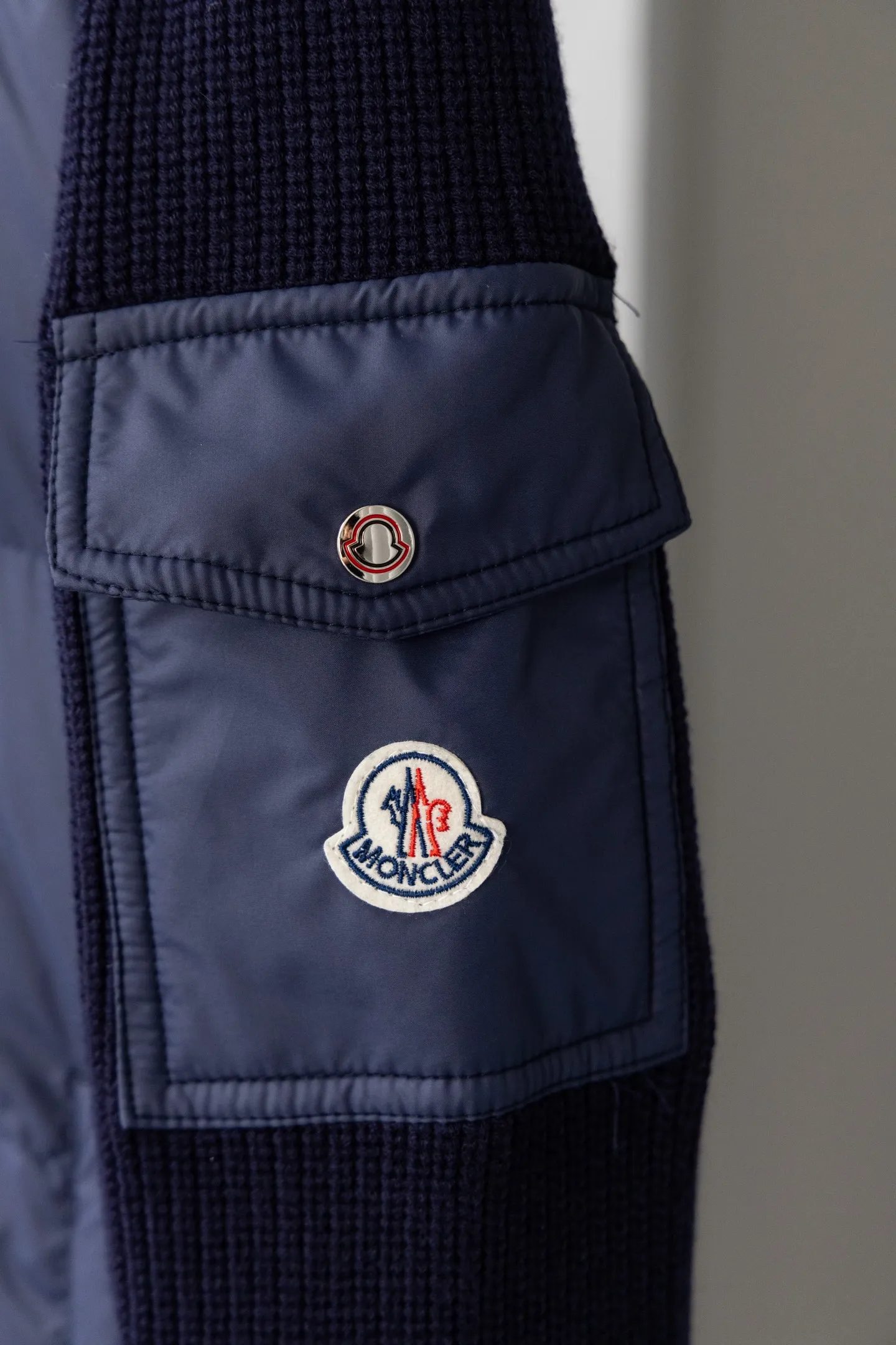 P560 Style number: M046 This is a knitted patchwork down jacket from Moncler. It combines the brand's high-end outdoor genes and fashion design. It is a luxurious item with both warmth and style in autumn and winter. Design highlights: Material splicing: Pure wool knitted sleeves are spliced ​​with a down front filled with 90 white duck down. The knitted part is soft and breathable, and the down part is fluffy and warm, achieving a dual fusion of style and function.  Detailed logo: The iconic Moncler badge pocket on the left arm is a classic embodiment of brand recognition; the stand-up collar design with a two-way zipper not only improves warmth, but also strengthens the neat styling.  Color embellishment: The contrasting red and blue stripes on the cuffs and hem inject vitality into the overall black tone, adding a retro college style charm. Craftsmanship and Quality: The down filling follows the European standard 90 down standard, with excellent fluffiness and down filling, with almost no stiff feeling. At the same time, it adopts the "line first and then separate down filling" process. The four-layer liner effectively prevents down from being drilled, and can maintain warmth even after long-term wear.  The knitted part is made of high-quality wool, which has a delicate touch and is not easily deformed. The splicing process with the down fabric is rigorous, showing a high-end texture level.  Style and Wearing This down jacket is based on the classic college style. The slim straight version can modify the body line and can be easily adapted to a variety of styles: it can be paired with jeans and casual shoes for a casual look on a daily basis. It can also be upgraded to an urban light luxury style by layering it with a turtleneck sweater inside and a suit outside. It is a key item in the winter wardrobe that is both practical and fashionable. Color: black, navy blue, sizes S-XL