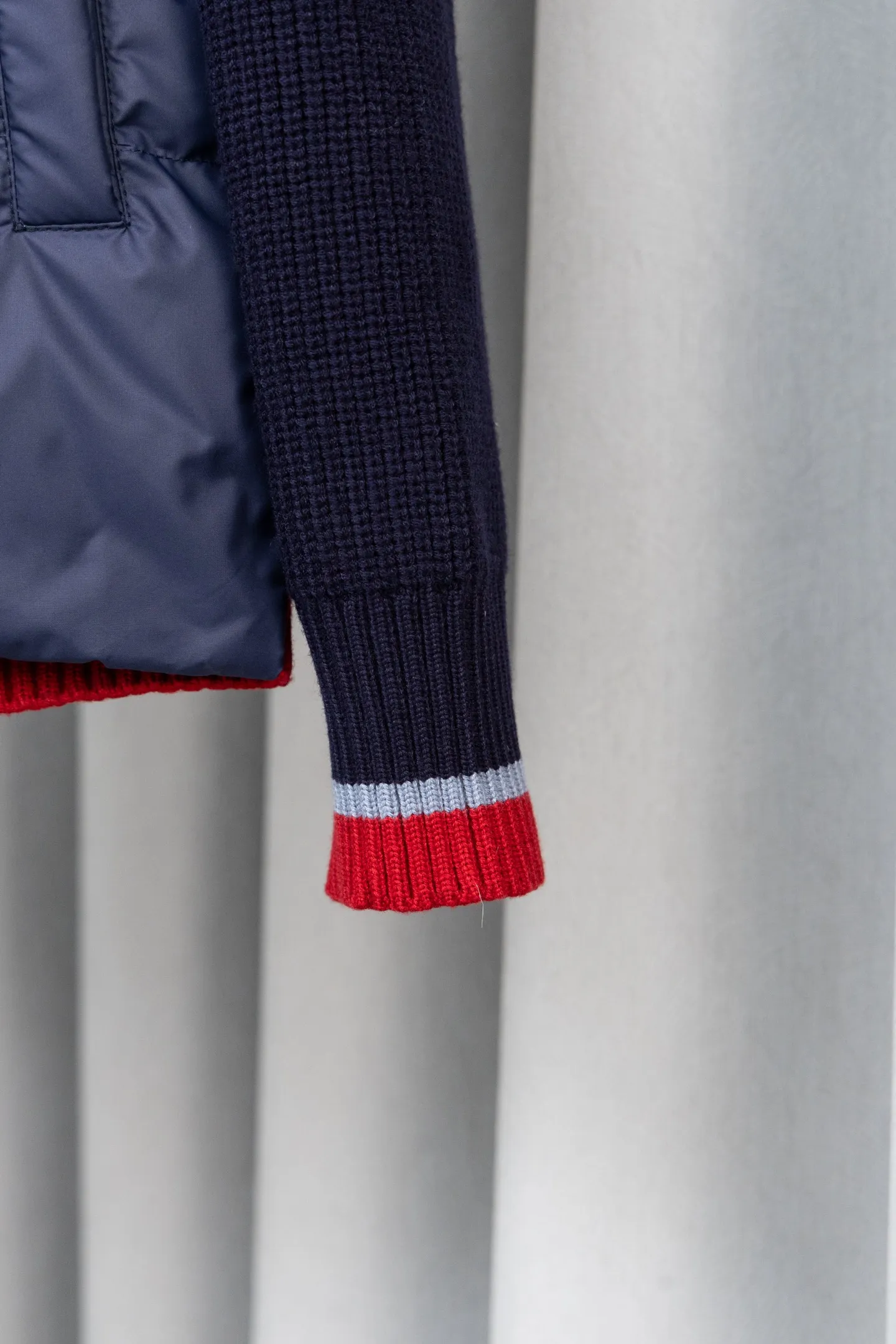 P560 Style number: M046 This is a knitted patchwork down jacket from Moncler. It combines the brand's high-end outdoor genes and fashion design. It is a luxurious item with both warmth and style in autumn and winter. Design highlights: Material splicing: Pure wool knitted sleeves are spliced ​​with a down front filled with 90 white duck down. The knitted part is soft and breathable, and the down part is fluffy and warm, achieving a dual fusion of style and function.  Detailed logo: The iconic Moncler badge pocket on the left arm is a classic embodiment of brand recognition; the stand-up collar design with a two-way zipper not only improves warmth, but also strengthens the neat styling.  Color embellishment: The contrasting red and blue stripes on the cuffs and hem inject vitality into the overall black tone, adding a retro college style charm. Craftsmanship and Quality: The down filling follows the European standard 90 down standard, with excellent fluffiness and down filling, with almost no stiff feeling. At the same time, it adopts the "line first and then separate down filling" process. The four-layer liner effectively prevents down from being drilled, and can maintain warmth even after long-term wear.  The knitted part is made of high-quality wool, which has a delicate touch and is not easily deformed. The splicing process with the down fabric is rigorous, showing a high-end texture level.  Style and Wearing This down jacket is based on the classic college style. The slim straight version can modify the body line and can be easily adapted to a variety of styles: it can be paired with jeans and casual shoes for a casual look on a daily basis. It can also be upgraded to an urban light luxury style by layering it with a turtleneck sweater inside and a suit outside. It is a key item in the winter wardrobe that is both practical and fashionable. Color: black, navy blue, sizes S-XL