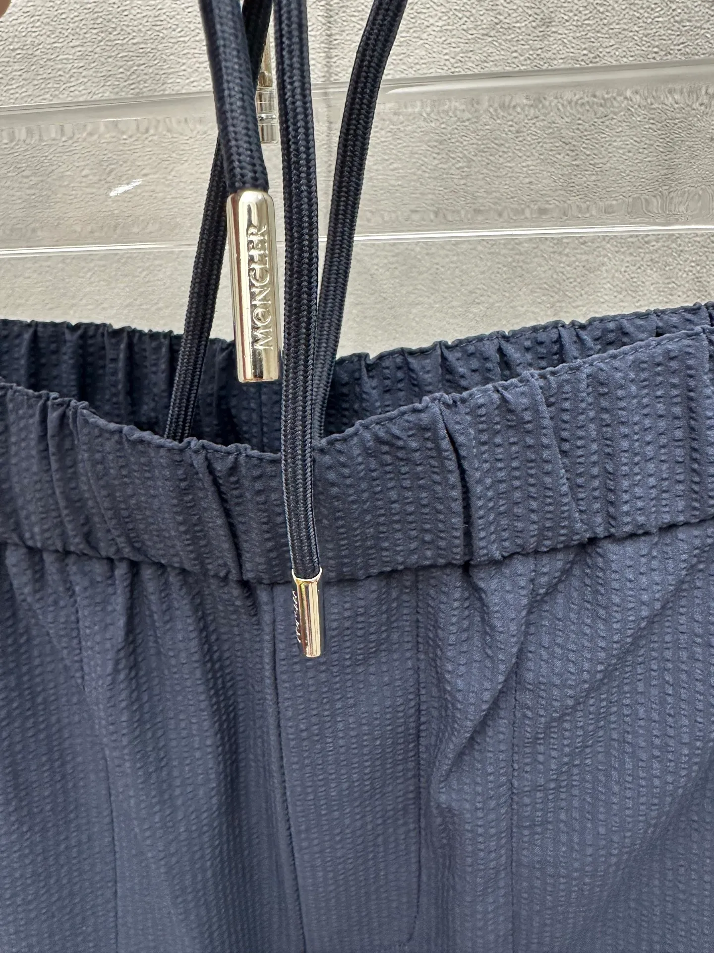 P400 MONCLER puff wrinkled trousers Fabric selection: Made of cotton blended woven fabric with 76% high cotton content + 24% polyester fiber. The high cotton content ensures that the fabric is soft, skin-friendly, and has good breathability. The addition of a small amount of polyester fiber balances the wrinkle resistance and elasticity of the overall fabric and greatly reduces its shrinkage. After preshrinking, dimensional changes during washing are negligible. The fusion of the two makes the fabric combine anti-wrinkle, quick-drying, easy care and other characteristics without losing the advantages of good wearing experience and strong breathability.  Bubble wrinkle technology: ground warp + bubble warp independent let-off. The bubble warp yarn feeding speed is about 20% higher than the ground warp yarn feeding speed. During weaving, the bubble warp is relaxed and accumulated, forming a naturally arched bubble unit. Through the alternating arrangement of yarns + floating length tissue changes, a clear grid frame is built between the bubble units, and finally the bubble three-dimensional effect and grid outline are locked through high-temperature heat setting.  Accessories: One-to-one customized drawstring head One-to-one customized LOGO labeling SIZE: 1 2 3 4