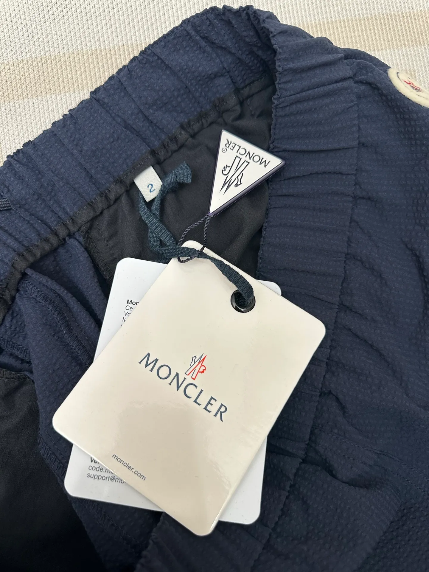 P400 MONCLER puff wrinkled trousers Fabric selection: Made of cotton blended woven fabric with 76% high cotton content + 24% polyester fiber. The high cotton content ensures that the fabric is soft, skin-friendly, and has good breathability. The addition of a small amount of polyester fiber balances the wrinkle resistance and elasticity of the overall fabric and greatly reduces its shrinkage. After preshrinking, dimensional changes during washing are negligible. The fusion of the two makes the fabric combine anti-wrinkle, quick-drying, easy care and other characteristics without losing the advantages of good wearing experience and strong breathability.  Bubble wrinkle technology: ground warp + bubble warp independent let-off. The bubble warp yarn feeding speed is about 20% higher than the ground warp yarn feeding speed. During weaving, the bubble warp is relaxed and accumulated, forming a naturally arched bubble unit. Through the alternating arrangement of yarns + floating length tissue changes, a clear grid frame is built between the bubble units, and finally the bubble three-dimensional effect and grid outline are locked through high-temperature heat setting.  Accessories: One-to-one customized drawstring head One-to-one customized LOGO labeling SIZE: 1 2 3 4