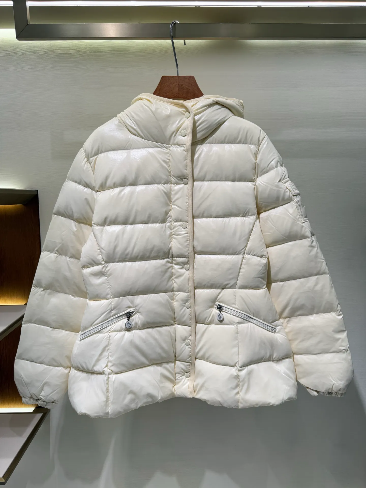 P1140 Moncler Barante series short waisted down jacket. The Barante down jacket is made of glossy nylon fabric and is inspired by the 1970s. The short version features a nipped-in waist and an A-line silhouette, highlighting a feminine style. An adjustable hood and signature logo patch add finishing touches.  Fabric: Made of nylon laque fabric, Nylon laque lining, filled with down (90 white goose down) Craftsmanship: Adjustable hood, zipper and snap closure, zipper pocket Adjustable cuffs (supports NFC function Color: black pink off-white Size: 0 1 2 3 4446080