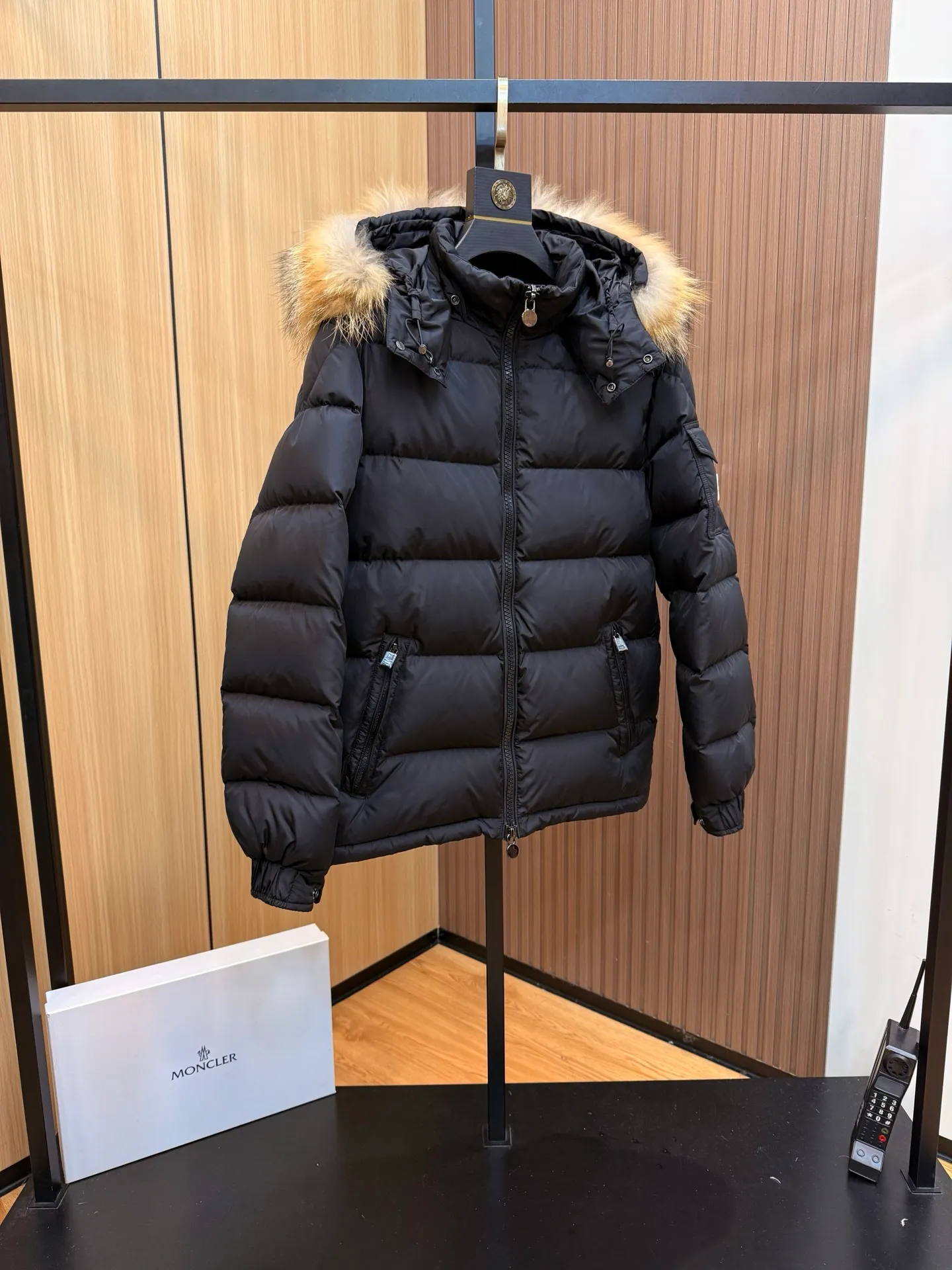 P1040 Moncler Mayaf short men's down jacket. The hood is removable. The fur collar is removable. Based on Maya, a removable fur collar is added. The Mayaf men's hooded down jacket is made of functional nylon fabric, and the hood is equipped with removable synthetic material trim.  The Mayaf short down jacket is a reinterpretation of the classic Moncler Maya style in an instantly recognizable silhouette, with a removable hood and adjustable hem. Made from functional fabric with removable synthetic trim on the hood. The sleeves are embellished with classic patch pockets, reflecting the brand's signature style. Details •Made from functional fabric •Technical fabric lining •Down-filled •Push-stud collar •Detachable hood with removable synthetic trim •Zip closure •Zip pockets •Patch pockets with press-stud •Adjustable elastic cuffs •Adjustable drawstring hem