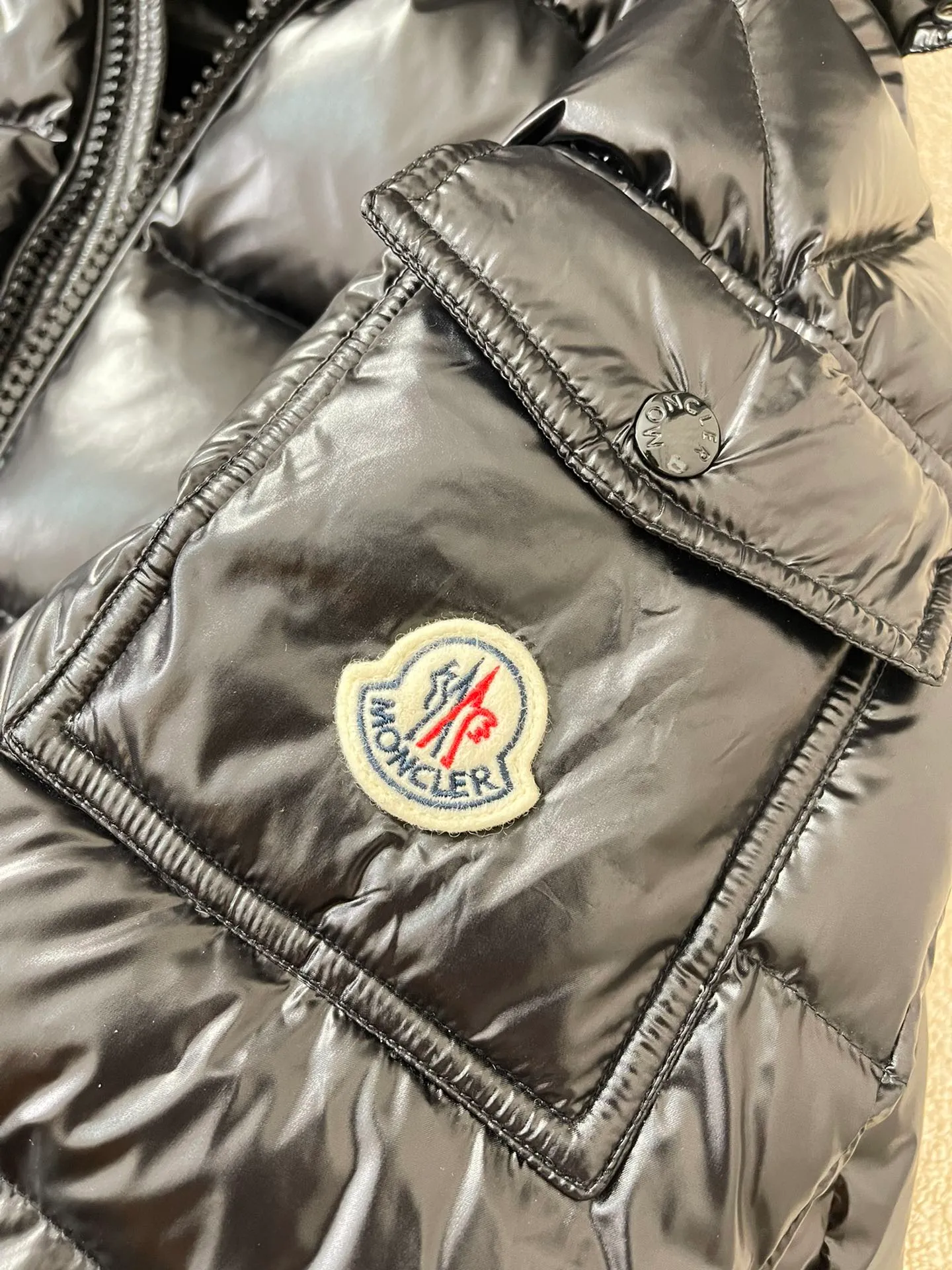 Flat detail P1180 Moncler Maya Men's Men's Short Down Jacket The Moncler Maya men's down jacket is made of shiny patented nylon with signature rectangular quilting, the epitome of Moncler style. A classic cropped design that transcends seasons and styles, it features a statement silhouette, removable hood and adjustable hem. The sleeves are embellished with classic patch pockets, showcasing the brand's signature style.  Fabric: 100% nylon, 90% white goose down Craftsmanship: Made of lacquered nylon, lacquered nylon lining filled with down, rectangular quilting, detachable hood with snaps that can be adjusted by drawstring, two-way zip fly, external and internal zippered pockets, adjustable elastic cuffs with snaps, hood with drawstring, sleeves with flap patch pockets, sleeves decorated with Moncler felt trademark.  Size: 123456 0548000