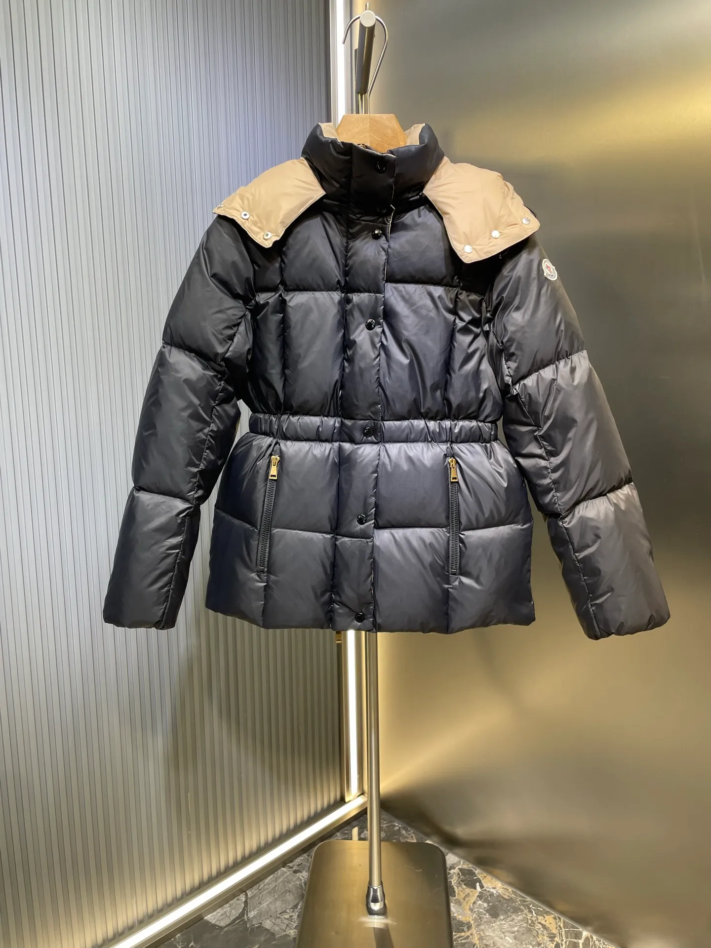 P910 MONCLER 25FW new autumn and winter product. Waisted black gold Agneux women's square quilted hooded short down jacket. The Agneux down jacket combines protective fabrics and exquisite textures. Short fit in functional nylon with a glossy satin finish. Paired with a nipped-in waist design, it outlines a feminine silhouette. Made of nylon Longue saison lining Filled with down Detachable and adjustable hood Zip and snap fastening Zippered pockets Elastic waist Black Apricot Sizes S M L