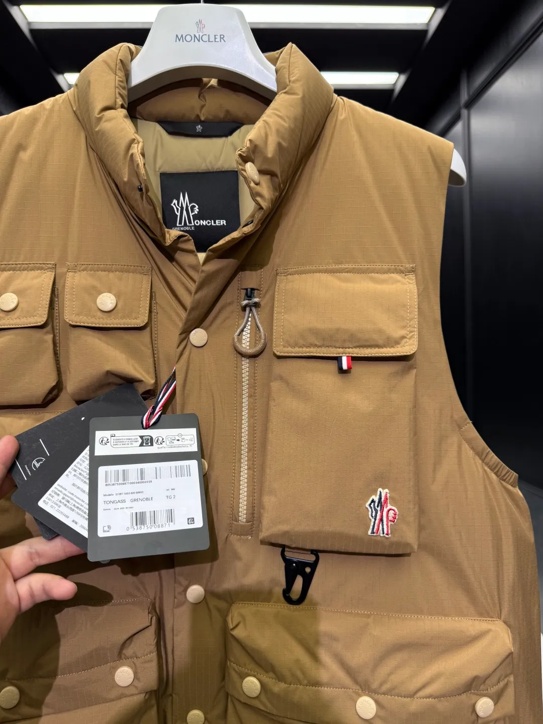 P820 ​​Premium Down ⬆️Moncler Grenoble Tongass Down Outdoor Vest. High-end Black Label Series. Original replacement fabric. Premium duck neck down filling. The Tongass Down Vest provides protection without being heavy and is specially designed for outdoor activities in mild weather.  The Tongass down vest is the result of research into lightweight performance outerwear. Functional fabric is tight and durable without adding extra weight. Features a large utility pocket and carabiner clip to reduce the amount of luggage you carry. Details •Designed for outdoor activities •Made from tight fabric •Polyester lining •Down filling •Snap button closure •Utility pockets with snap, zip and Velcro closure •Drawstring hem •Front carabiner •Reflective details Size: 1-5 Light Brown/Black D00780