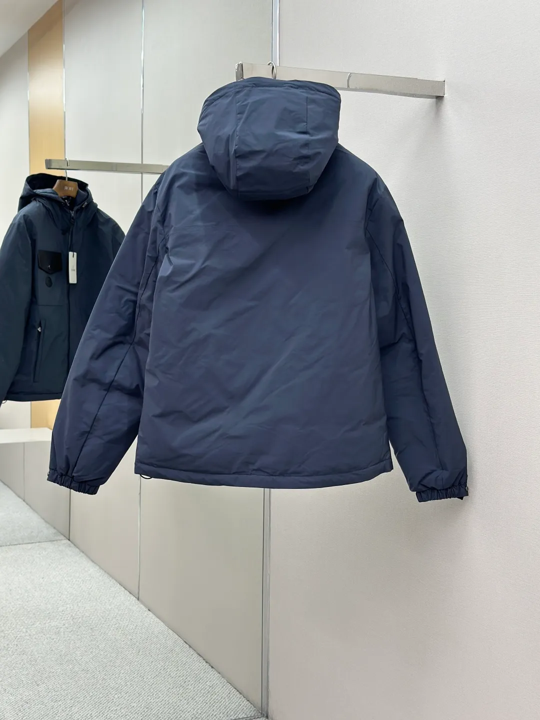 P890 MONCLER hooded jacket-style down jacket is made of 100% polyester fiber. After microfiberization treatment, the individual fibers become extremely fine, which greatly increases the fiber surface area, making the fabric soft and smooth, and the touch is close to natural fibers. The high-density textile method makes the structure tight, thus giving it a certain degree of wrinkle resistance, windproof warmth and wear resistance.  Lining selection: High-density lining fabric made of ultra-fine denier, 0.08mm thickness to avoid increasing the overall weight and making it smooth to wear. The high-density woven structure forms a wind resistance layer to protect the thermal efficiency of the thermal layer from loss. It can also withstand the expansion pressure of down and prevent deformation and damage after long-term use.  High-quality filling: 90 white duck down is selected, with a weight of 200g, ensuring excellent thermal insulation performance. After strict screening and treatment, the velvet is not easy to be drilled, ensuring durability. Details: The leather flap pocket on the chest is matched with a pebbled leather flap + matte metal buckle. It is low-key and exudes nobility. The hidden adjustment rope gives a sense of sophistication when you raise your hand. The "ID card" is directly embedded on the black satin inner patch pocket! Silver snaps + red, white and blue webbing, low-key yet exuding a sense of luxury, both visually and tactilely smooth.  Accessories: one-to-one customized buttons, one-to-one customized hem drawstring buckle, one-to-one customized phoenix eyes, one-to-one customized zipper pendant SIZE: 1 2 3 4