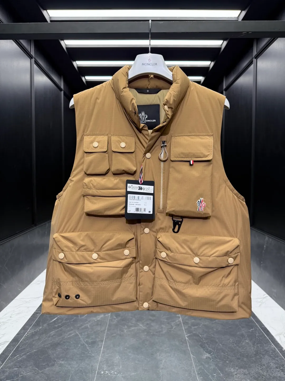 P860 Premium Down⬆️Moncler Grenoble Tongass Down Outdoor Vest. High-end Black Label Series. Original replacement fabric. Premium gooseneck filling. 🎁 Comes standard with a full set of counter gift box packaging. Upgraded original magnetic gift box. The Tongass Down Vest provides protection without being heavy, and is specially designed for outdoor activities in mild weather.  The Tongass down vest is the result of research into lightweight performance outerwear. Functional fabric is tight and durable without adding extra weight. Features a large utility pocket and carabiner clip to reduce the amount of luggage you carry. Details •Designed for outdoor activities •Made from tight fabric •Polyester lining •Down filling •Snap button closure •Utility pockets with snap, zip and Velcro closure •Drawstring hem •Front carabiner •Reflective details Size: 1-5 Cream/Light Brown/Black D00780