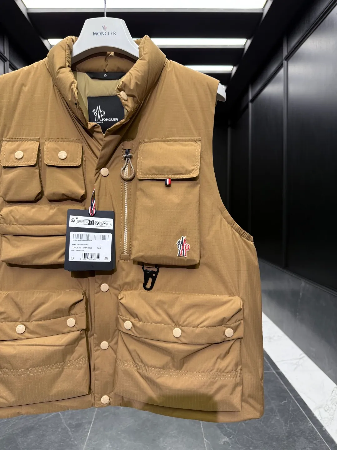 P860 Premium Down⬆️Moncler Grenoble Tongass Down Outdoor Vest. High-end Black Label Series. Original replacement fabric. Premium gooseneck filling. 🎁 Comes standard with a full set of counter gift box packaging. Upgraded original magnetic gift box. The Tongass Down Vest provides protection without being heavy, and is specially designed for outdoor activities in mild weather.  The Tongass down vest is the result of research into lightweight performance outerwear. Functional fabric is tight and durable without adding extra weight. Features a large utility pocket and carabiner clip to reduce the amount of luggage you carry. Details •Designed for outdoor activities •Made from tight fabric •Polyester lining •Down filling •Snap button closure •Utility pockets with snap, zip and Velcro closure •Drawstring hem •Front carabiner •Reflective details Size: 1-5 Cream/Light Brown/Black D00780