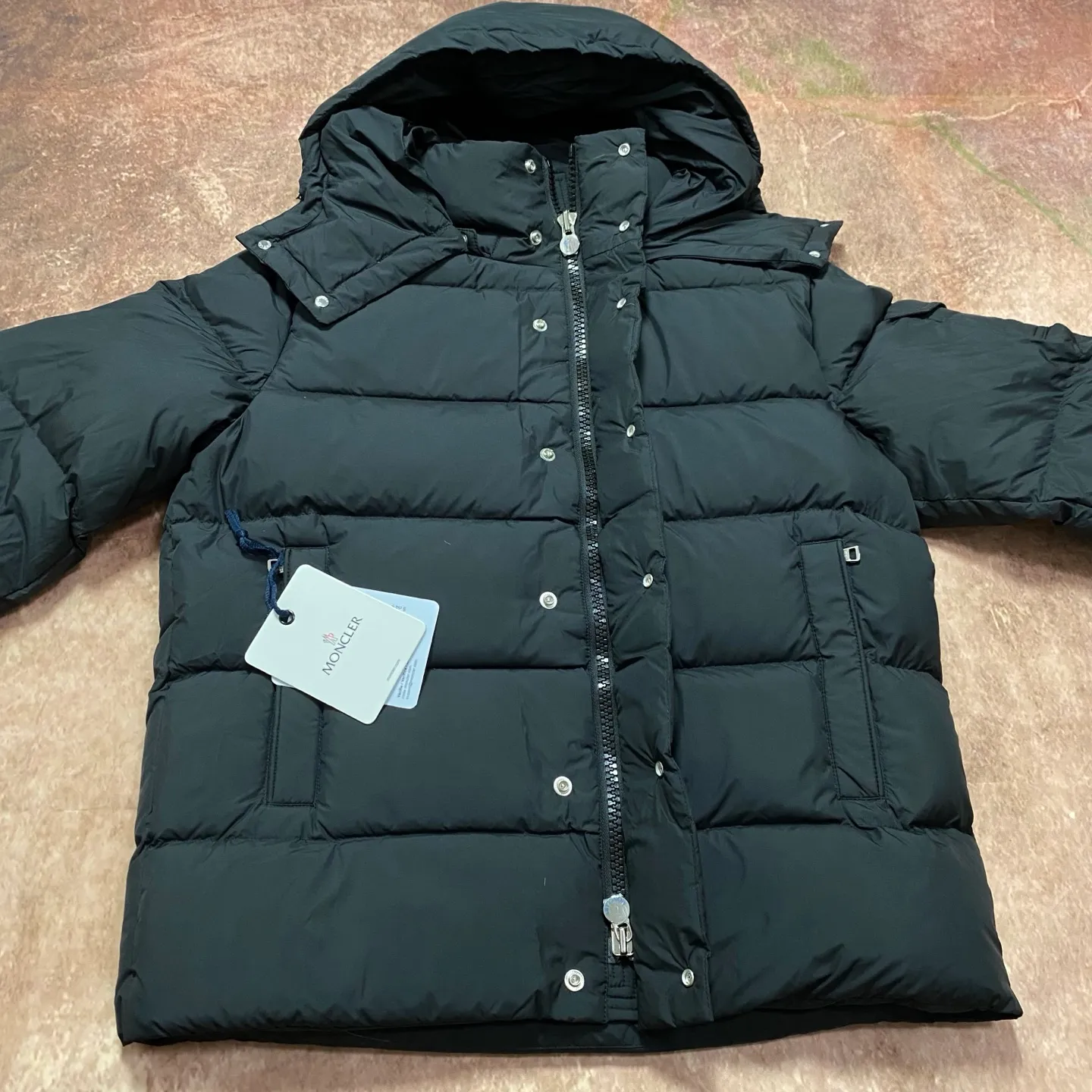 P840 MONCLER matte Maya down jacket. Process description: Made of the brand's iconic longue saison fabric, it has both light texture and excellent thermal insulation performance. This unisex down jacket has a matte appearance and is lined with lon léger brillant material to ensure comfort. Its core filling is 90% high-quality goose down, with a down filling capacity of 204 grams, providing excellent thermal insulation effect. The design continues the classic elements of Moner, with the short silhouette and sleeve patch pocket details paying tribute to the Maya series. In terms of functionality, it is equipped with a detachable and adjustable hood, a dual zipper and snap button opening system, and a zipper pocket to enhance practicality. The sleeves are specially designed with adjustable cuffs and a drawstring hem design, so you can freely adjust the tightness according to your needs. The overall craftsmanship is exquisite, which not only retains Moner's consistent fashion genes, but also enhances the convenience of daily wear through exquisite detail processing. ⚠️Color: Black ⚠️Size: 12345