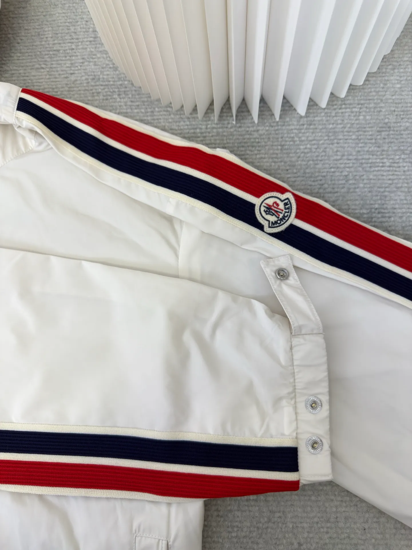 P570 MONCLER lightweight jacket with web trim at the mouth is made of 100% polyester fiber to create a tough protective outer layer. It is famous for its excellent tear resistance and wear resistance. It can quickly return to flatness during wearing and maintain the crisp and stylish appearance of the clothing for a long time. At the same time, it is not easy to deform after being washed for a long time.  Decorative edging in two different colors has been added to the center section of the sleeves. This design element not only adds visual highlights to clothing, making it more fashionable and unique. The webbing is precisely positioned along the cuffs to the seam of the collar and hat to ensure symmetry and overall smoothness. Before actual sewing, use very fine basting stitches for pre-fixing. This step is crucial to prevent the webbing from slipping, twisting, or wrinkling during sewing and ensuring that the final stitch is straight and perfect. Size 1 2 3 4