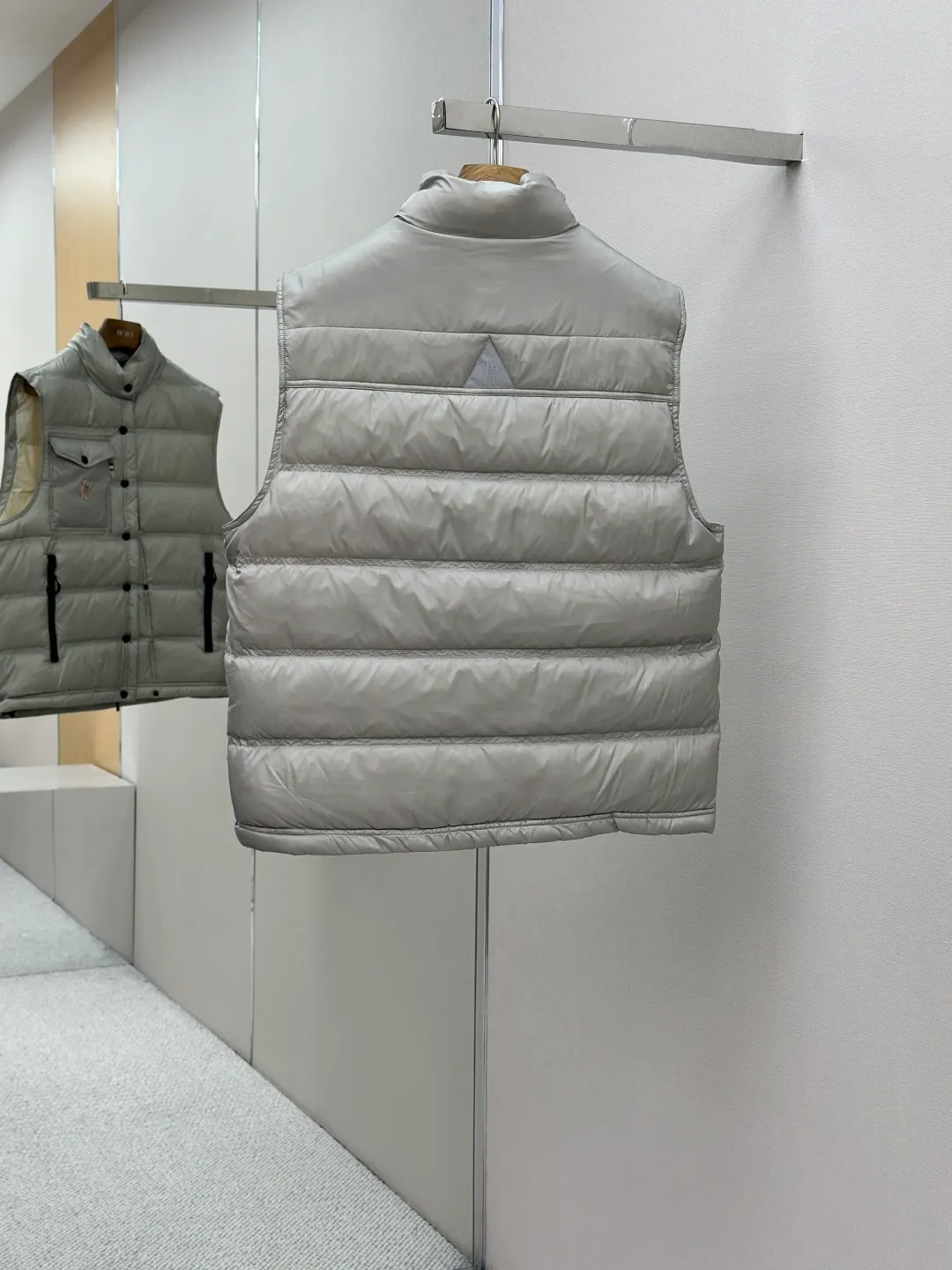 P680 MONCLER down vest with reflective markings Fabric selection: Made of ultra-fine nylon yarn woven in a high-density manner. The number of yarns per unit area is large, and the gaps between the yarns are very small, which can effectively block the penetration of cold wind. The fine weave keeps it lightweight and soft to the touch, physically restricting the lightweight down fibers from slipping through the gaps. Nylon fiber itself has good wear resistance and is not easy to snag, which significantly extends its service life and can easily cope with the needs of multiple scenarios.  Lining selection: The lining is made of 100% polyester fiber high-density weaving. The thickness of 0.08mm avoids increasing the overall weight and makes it smooth to wear. The high-density weaving structure forms a wind resistance layer to protect the thermal efficiency of the thermal insulation layer from loss. At the same time, it can withstand the expansion pressure of down and prevent deformation and damage after long-term use.  High-quality filling: 90 white duck down is selected, with a weight of 130g, ensuring excellent thermal insulation performance. After strict screening and processing, the velvet is not easy to get drilled, ensuring durability.  Process: Through the reflective cloth punching process, the logo is regularly arranged on the triangular reflective mark with dozens of small holes, which not only improves the functionality, but also strengthens the recognition and aesthetics.   Accessories: Customized snap buttons, customized zipper pullers, customized badges, customized elastic buckles, etc. SIZE: 1 2 3 4