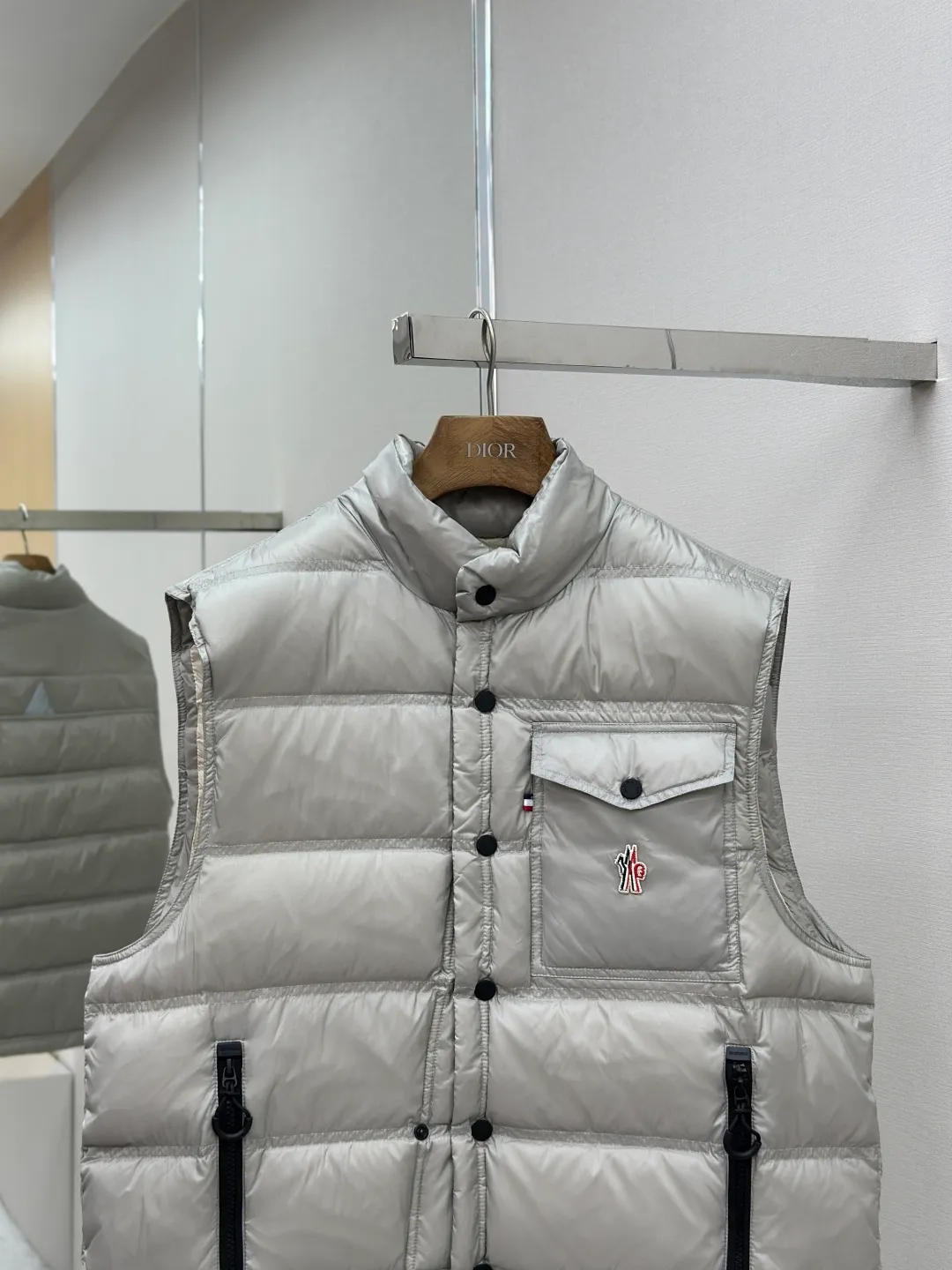 P680 MONCLER down vest with reflective markings Fabric selection: Made of ultra-fine nylon yarn woven in a high-density manner. The number of yarns per unit area is large, and the gaps between the yarns are very small, which can effectively block the penetration of cold wind. The fine weave keeps it lightweight and soft to the touch, physically restricting the lightweight down fibers from slipping through the gaps. Nylon fiber itself has good wear resistance and is not easy to snag, which significantly extends its service life and can easily cope with the needs of multiple scenarios.  Lining selection: The lining is made of 100% polyester fiber high-density weaving. The thickness of 0.08mm avoids increasing the overall weight and makes it smooth to wear. The high-density weaving structure forms a wind resistance layer to protect the thermal efficiency of the thermal insulation layer from loss. At the same time, it can withstand the expansion pressure of down and prevent deformation and damage after long-term use.  High-quality filling: 90 white duck down is selected, with a weight of 130g, ensuring excellent thermal insulation performance. After strict screening and processing, the velvet is not easy to get drilled, ensuring durability.  Process: Through the reflective cloth punching process, the logo is regularly arranged on the triangular reflective mark with dozens of small holes, which not only improves the functionality, but also strengthens the recognition and aesthetics.   Accessories: Customized snap buttons, customized zipper pullers, customized badges, customized elastic buckles, etc. SIZE: 1 2 3 4