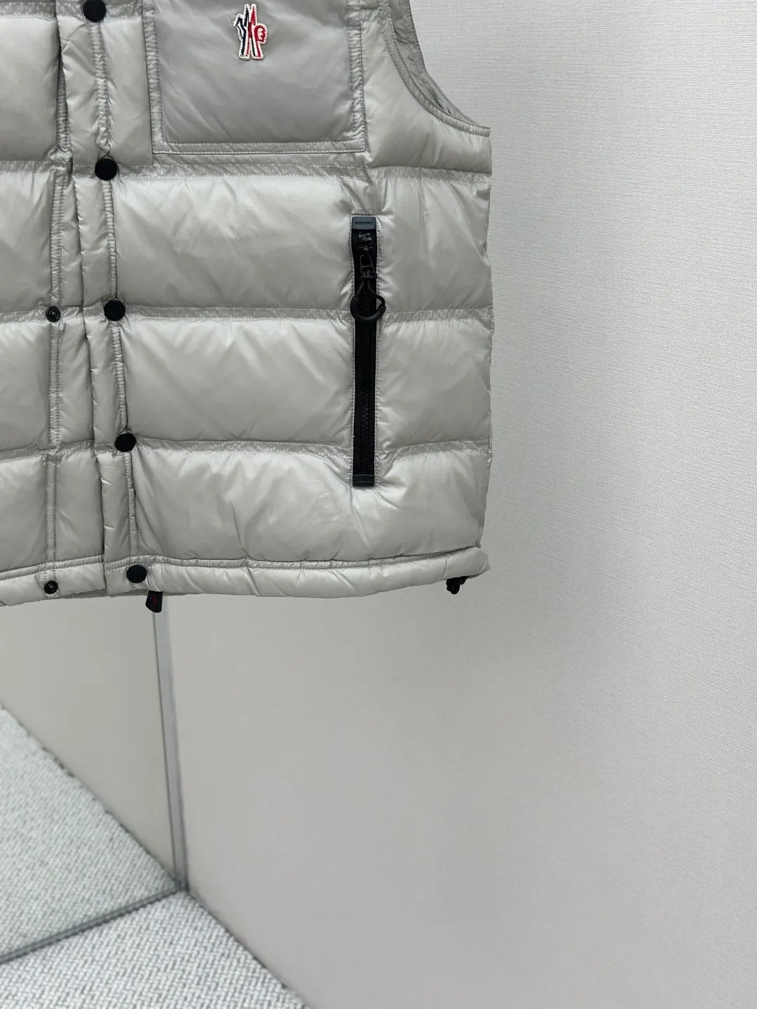 P680 MONCLER down vest with reflective markings Fabric selection: Made of ultra-fine nylon yarn woven in a high-density manner. The number of yarns per unit area is large, and the gaps between the yarns are very small, which can effectively block the penetration of cold wind. The fine weave keeps it lightweight and soft to the touch, physically restricting the lightweight down fibers from slipping through the gaps. Nylon fiber itself has good wear resistance and is not easy to snag, which significantly extends its service life and can easily cope with the needs of multiple scenarios.  Lining selection: The lining is made of 100% polyester fiber high-density weaving. The thickness of 0.08mm avoids increasing the overall weight and makes it smooth to wear. The high-density weaving structure forms a wind resistance layer to protect the thermal efficiency of the thermal insulation layer from loss. At the same time, it can withstand the expansion pressure of down and prevent deformation and damage after long-term use.  High-quality filling: 90 white duck down is selected, with a weight of 130g, ensuring excellent thermal insulation performance. After strict screening and processing, the velvet is not easy to get drilled, ensuring durability.  Process: Through the reflective cloth punching process, the logo is regularly arranged on the triangular reflective mark with dozens of small holes, which not only improves the functionality, but also strengthens the recognition and aesthetics.   Accessories: Customized snap buttons, customized zipper pullers, customized badges, customized elastic buckles, etc. SIZE: 1 2 3 4