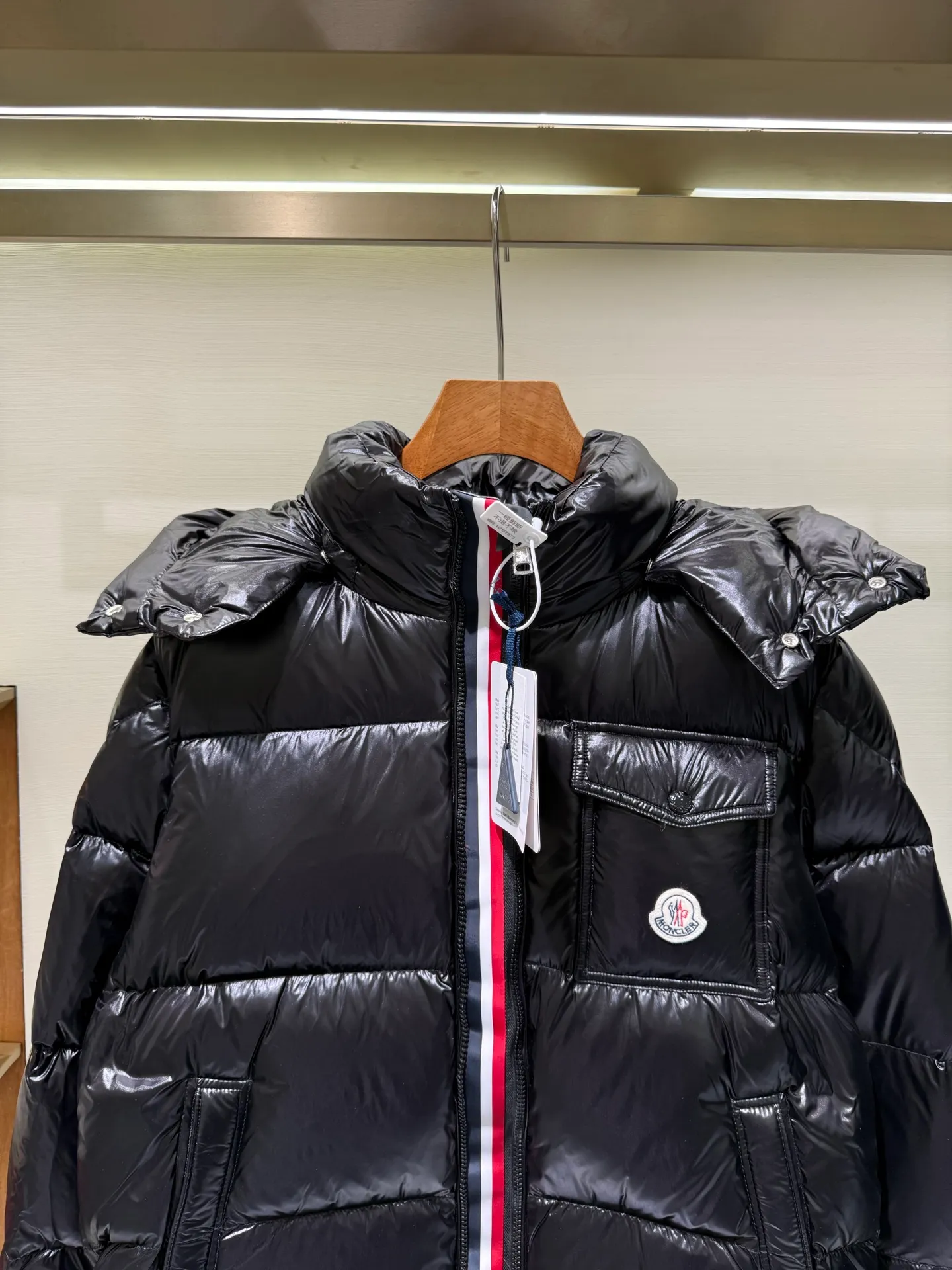 P1180 Moncler Montbeliard glossy down jacket The Montbeliard down jacket is made of shiny patent nylon and features highly recognizable rectangular quilting. Featuring a hooded design and signature patch pocket at chest.  Fabric: 100% nylon Filling content: 90% white goose down 250-300g Craftsmanship: Made of nylon laqué fabric Nylon laque lining Filled with down, detachable and adjustable hood with drawstring closure Built-in flap with webbing, black pocket details at the lower end Zipper closure Collar with snap buttons Zipper pockets Patch pockets with snap buttons Adjustable cuffs Adjustable elastic drawstring hem.  Size: 1 2 3 4 5 0548000