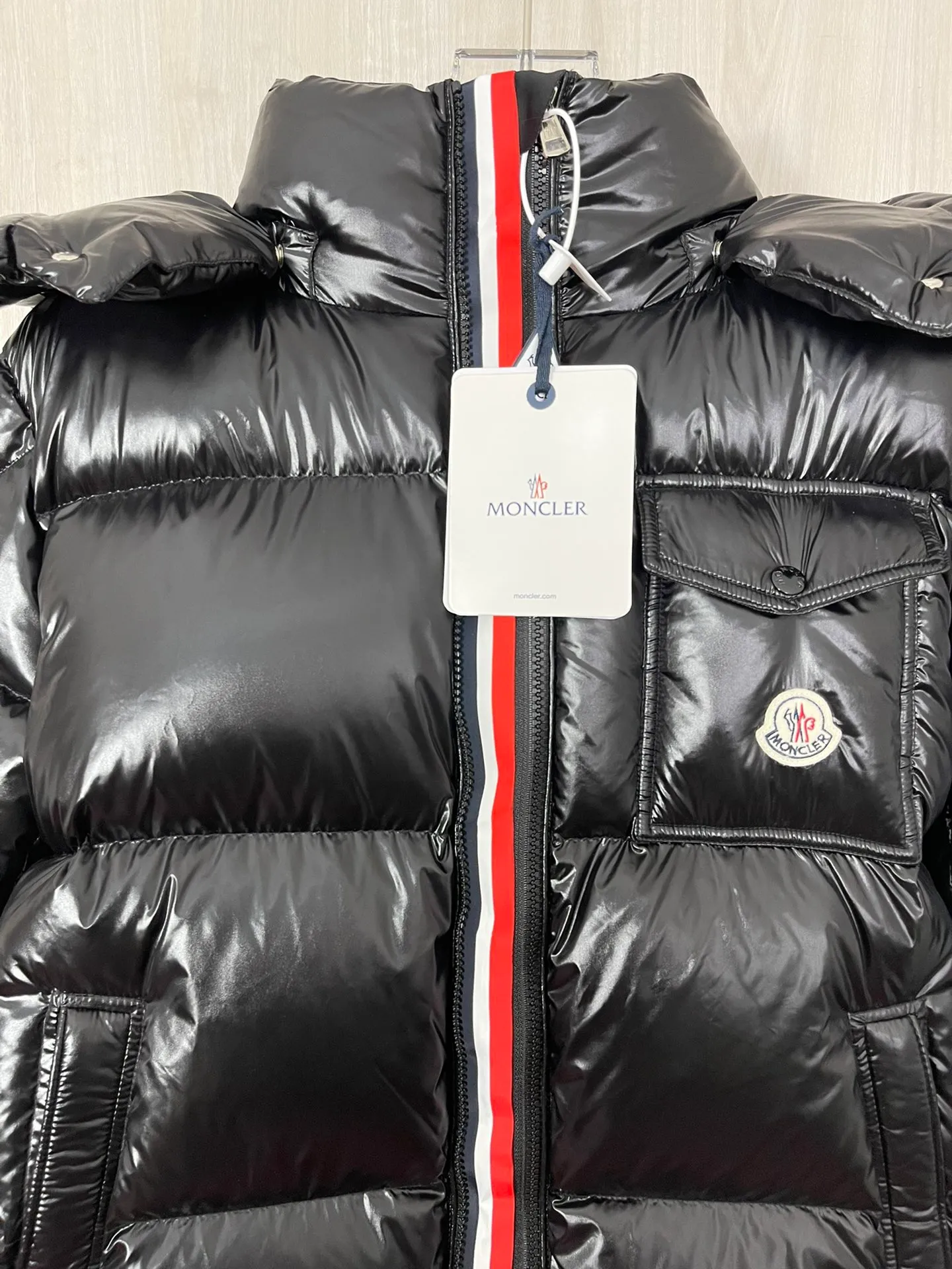 P1180 Moncler Montbeliard glossy down jacket The Montbeliard down jacket is made of shiny patent nylon and features highly recognizable rectangular quilting. Featuring a hooded design and signature patch pocket at chest.  Fabric: 100% nylon Filling content: 90% white goose down 250-300g Craftsmanship: Made of nylon laqué fabric Nylon laque lining Filled with down, detachable and adjustable hood with drawstring closure Built-in flap with webbing, black pocket details at the lower end Zipper closure Collar with snap buttons Zipper pockets Patch pockets with snap buttons Adjustable cuffs Adjustable elastic drawstring hem.  Size: 1 2 3 4 5 0548000