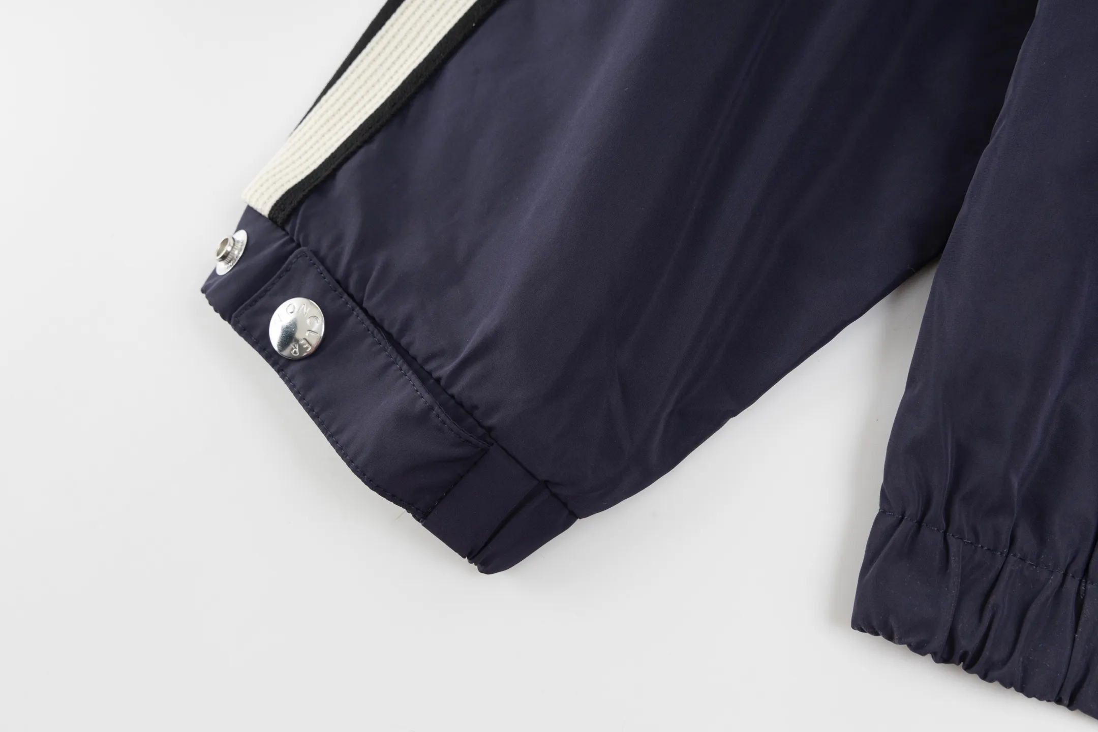P550 Exclusive supply] Moncler Webbing Armband Lightweight Jacket (Navy Blue) The fabric is made of 100% polyester fiber to create a tough protective outer layer. It is known for its excellent tear resistance and wear resistance. It can quickly return to flatness during wearing and maintain the crisp and stylish appearance of the clothing for a long time. At the same time, it is not easy to deform after being washed for a long time. Decorative edging in two different colors has been added to the center section of the sleeves. This design element not only adds visual highlights to the clothing, making it more fashionable and unique, the webbing is precisely positioned along the specified contours from the cuffs to the seam of the collar to ensure symmetry and overall smoothness. Before actual sewing, use very fine basting stitches for pre-fixing. This step is crucial to prevent the webbing from slipping, twisting, or wrinkling during sewing and ensuring that the final stitch is straight and perfect. Size:1/2/3/4