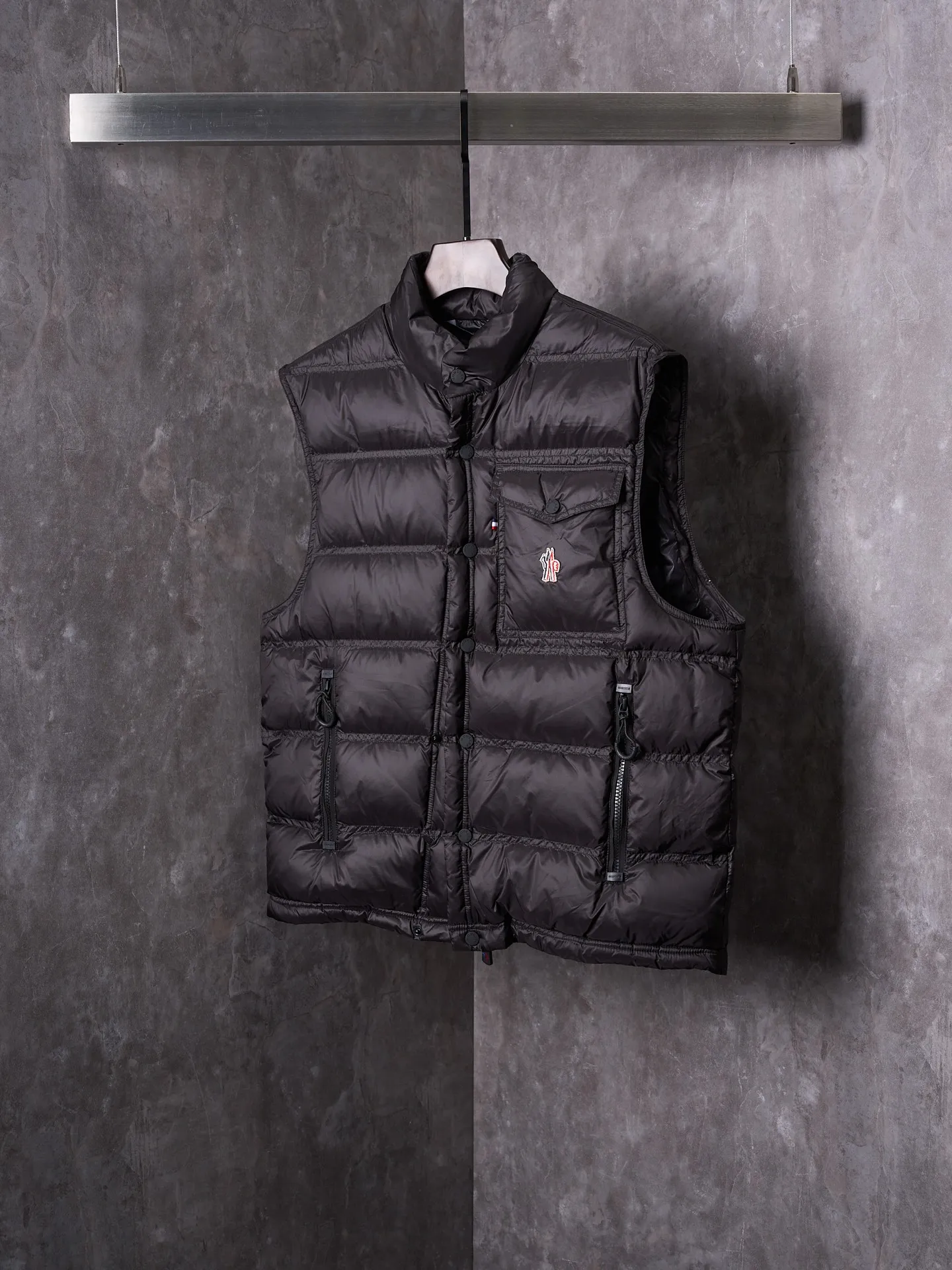 P680 Actual hanging auction] MONCLER/Mandow embroidered reflective logo stand-up collar down vest [Ready stock] 1 2 3 4 It is made of extremely fine nylon yarn and woven in a high-density way. The number of yarns per unit area is large, and the gaps between the yarns are very small, which can effectively block the penetration of cold wind. The fine weave keeps it lightweight and soft to the touch, physically restricting the lightweight down fibers from slipping through the gaps. Nylon fiber itself has good wear resistance and is not easy to snag, which significantly extends its service life and can easily cope with the needs of multiple scenarios.  The lining is made of high-density weaving of 100% polyester fiber, with a thickness of 0.08mm to avoid increasing the overall weight and making it smooth to wear. The high-density weaving structure forms a wind resistance layer to protect the thermal efficiency of the thermal layer from loss. It can withstand the expansion pressure of down and prevent deformation and damage after long-term use.  It uses 90 white duck down with a weight of 130g to ensure excellent thermal insulation performance. After strict screening and processing, the velvet is not easy to get drilled, ensuring durability.  Through the reflective cloth punching process, the logo is regularly arranged on the triangular reflective mark with dozens of small holes, which not only improves functionality but also enhances recognition and aesthetics.