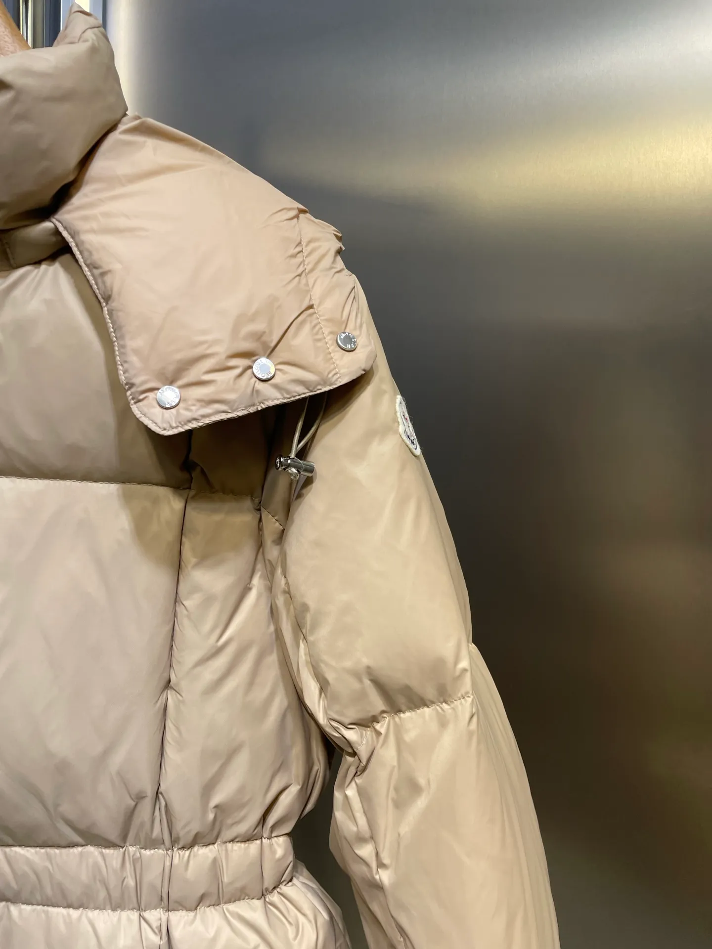 P910 MONCLER 25FW new autumn and winter product. Waisted black gold Agneux women's square quilted hooded short down jacket. The Agneux down jacket combines protective fabrics and exquisite textures. Short fit in functional nylon with a glossy satin finish. Paired with a nipped-in waist design, it outlines a feminine silhouette. Made of nylon Longue saison lining Filled with down Detachable and adjustable hood Zip and snap fastening Zippered pockets Elastic waist Black Apricot Sizes S M L