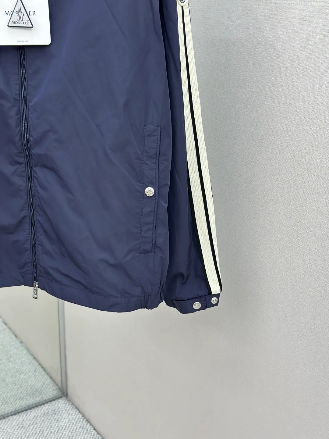 P560 MONCLER web-trimmed lightweight jacket Fabric selection: 100% polyester fiber is used to create a tough protective outer layer. It is known for its excellent tear resistance and wear resistance. It can quickly return to flatness during wearing and maintain the crisp and stylish appearance of the clothing for a long time. At the same time, it is not easy to deform after being washed for a long time.   Features: Two different colored decorative strips added to the center part of the sleeves. This design element can not only add visual highlights to clothing, making it more fashionable and unique. Craftsmanship: The webbing is precisely positioned along the cuffs to the seam of the collar and hat to ensure symmetry and overall smoothness. Before actual sewing, use very fine basting stitches for pre-fixing. This step is crucial to prevent the webbing from slipping, twisting, or wrinkling during sewing and ensuring that the final stitch is straight and perfect.  Accessories: Custom zipper puller, custom buttons with logo, custom hood drawstring elastic buckle SIZE: 1 2 3 4
