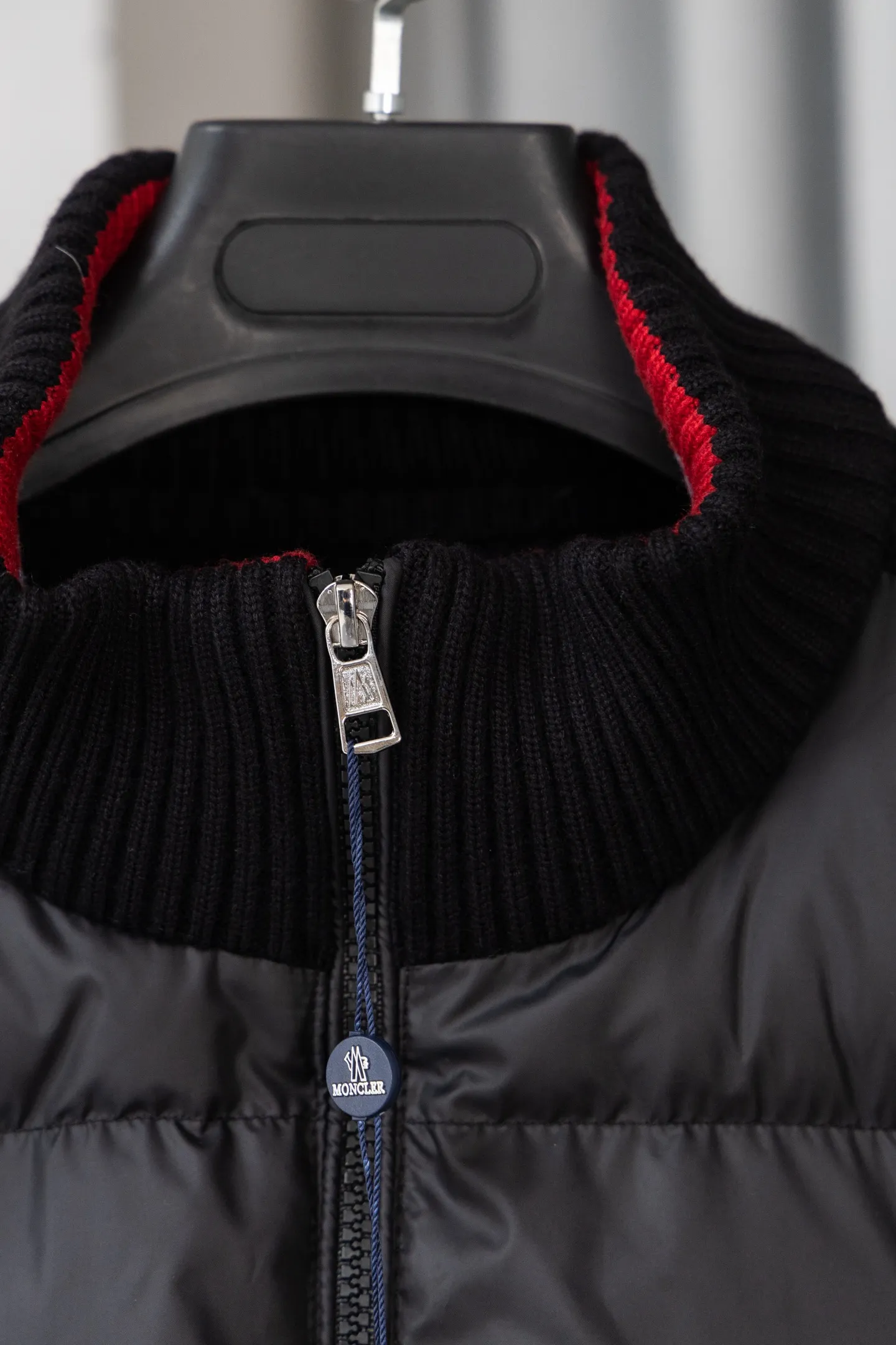 P560 Style number: M046 This is a knitted patchwork down jacket from Moncler. It combines the brand's high-end outdoor genes and fashion design. It is a luxurious item with both warmth and style in autumn and winter. Design highlights: Material splicing: Pure wool knitted sleeves are spliced ​​with a down front filled with 90 white duck down. The knitted part is soft and breathable, and the down part is fluffy and warm, achieving a dual fusion of style and function.  Detailed logo: The iconic Moncler badge pocket on the left arm is a classic embodiment of brand recognition; the stand-up collar design with a two-way zipper not only improves warmth, but also strengthens the neat styling.  Color embellishment: The contrasting red and blue stripes on the cuffs and hem inject vitality into the overall black tone, adding a retro college style charm. Craftsmanship and Quality: The down filling follows the European standard 90 down standard, with excellent fluffiness and down filling, with almost no stiff feeling. At the same time, it adopts the "line first and then separate down filling" process. The four-layer liner effectively prevents down from being drilled, and can maintain warmth even after long-term wear.  The knitted part is made of high-quality wool, which has a delicate touch and is not easily deformed. The splicing process with the down fabric is rigorous, showing a high-end texture level.  Style and Wearing This down jacket is based on the classic college style. The slim straight version can modify the body line and can be easily adapted to a variety of styles: it can be paired with jeans and casual shoes for a casual look on a daily basis. It can also be upgraded to an urban light luxury style by layering it with a turtleneck sweater inside and a suit outside. It is a key item in the winter wardrobe that is both practical and fashionable. Color: black, navy blue, sizes S-XL