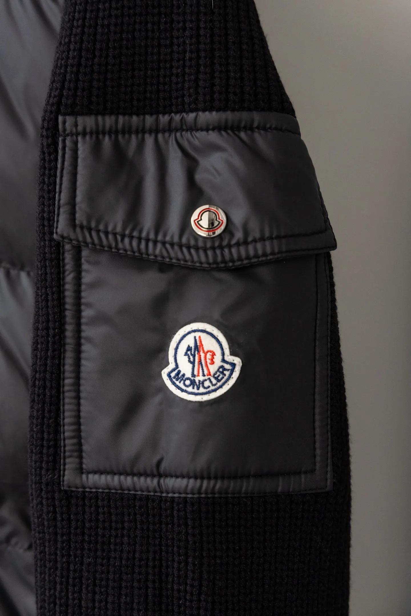 P560 Style number: M046 This is a knitted patchwork down jacket from Moncler. It combines the brand's high-end outdoor genes and fashion design. It is a luxurious item with both warmth and style in autumn and winter. Design highlights: Material splicing: Pure wool knitted sleeves are spliced ​​with a down front filled with 90 white duck down. The knitted part is soft and breathable, and the down part is fluffy and warm, achieving a dual fusion of style and function.  Detailed logo: The iconic Moncler badge pocket on the left arm is a classic embodiment of brand recognition; the stand-up collar design with a two-way zipper not only improves warmth, but also strengthens the neat styling.  Color embellishment: The contrasting red and blue stripes on the cuffs and hem inject vitality into the overall black tone, adding a retro college style charm. Craftsmanship and Quality: The down filling follows the European standard 90 down standard, with excellent fluffiness and down filling, with almost no stiff feeling. At the same time, it adopts the "line first and then separate down filling" process. The four-layer liner effectively prevents down from being drilled, and can maintain warmth even after long-term wear.  The knitted part is made of high-quality wool, which has a delicate touch and is not easily deformed. The splicing process with the down fabric is rigorous, showing a high-end texture level.  Style and Wearing This down jacket is based on the classic college style. The slim straight version can modify the body line and can be easily adapted to a variety of styles: it can be paired with jeans and casual shoes for a casual look on a daily basis. It can also be upgraded to an urban light luxury style by layering it with a turtleneck sweater inside and a suit outside. It is a key item in the winter wardrobe that is both practical and fashionable. Color: black, navy blue, sizes S-XL