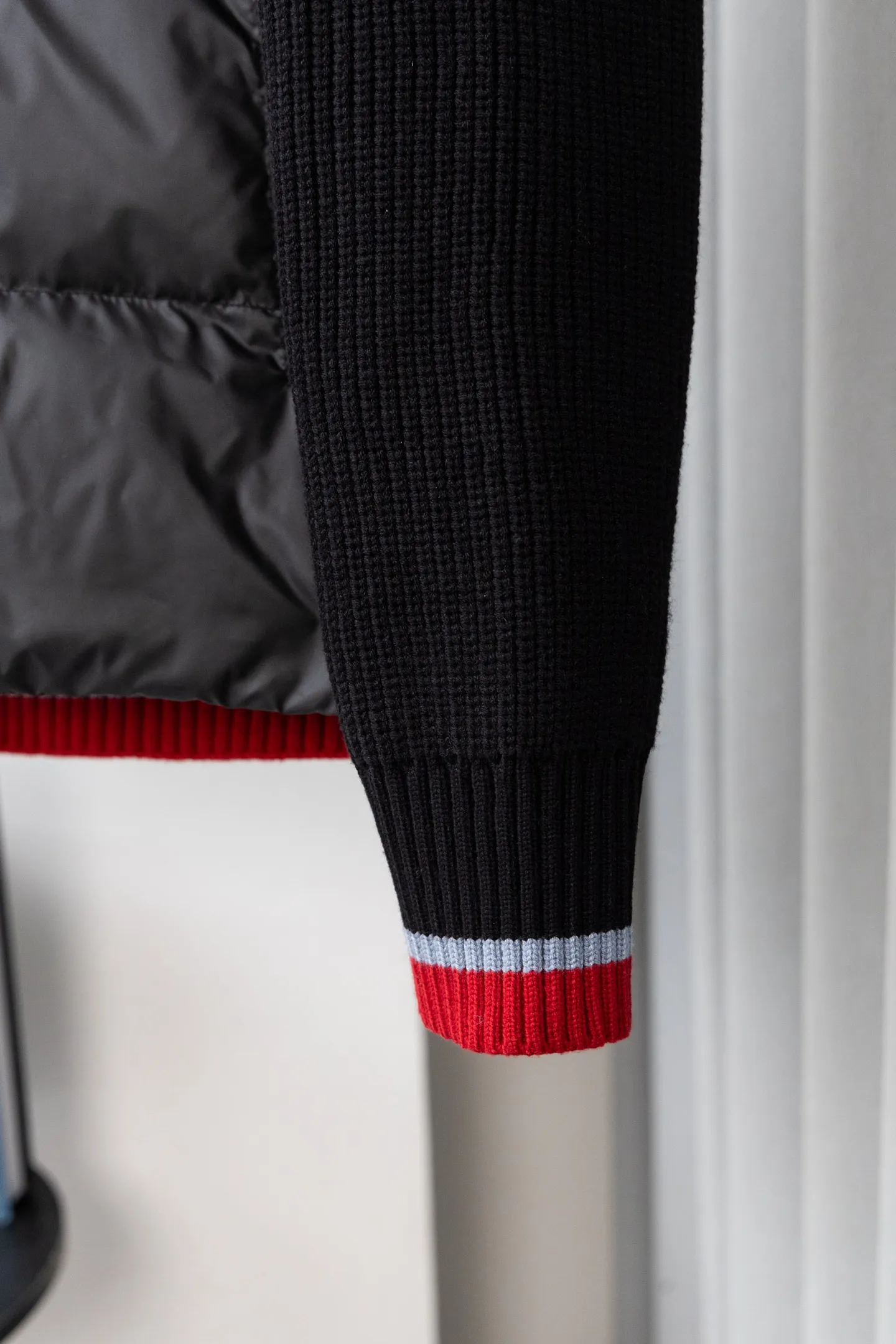 P560 Style number: M046 This is a knitted patchwork down jacket from Moncler. It combines the brand's high-end outdoor genes and fashion design. It is a luxurious item with both warmth and style in autumn and winter. Design highlights: Material splicing: Pure wool knitted sleeves are spliced ​​with a down front filled with 90 white duck down. The knitted part is soft and breathable, and the down part is fluffy and warm, achieving a dual fusion of style and function.  Detailed logo: The iconic Moncler badge pocket on the left arm is a classic embodiment of brand recognition; the stand-up collar design with a two-way zipper not only improves warmth, but also strengthens the neat styling.  Color embellishment: The contrasting red and blue stripes on the cuffs and hem inject vitality into the overall black tone, adding a retro college style charm. Craftsmanship and Quality: The down filling follows the European standard 90 down standard, with excellent fluffiness and down filling, with almost no stiff feeling. At the same time, it adopts the "line first and then separate down filling" process. The four-layer liner effectively prevents down from being drilled, and can maintain warmth even after long-term wear.  The knitted part is made of high-quality wool, which has a delicate touch and is not easily deformed. The splicing process with the down fabric is rigorous, showing a high-end texture level.  Style and Wearing This down jacket is based on the classic college style. The slim straight version can modify the body line and can be easily adapted to a variety of styles: it can be paired with jeans and casual shoes for a casual look on a daily basis. It can also be upgraded to an urban light luxury style by layering it with a turtleneck sweater inside and a suit outside. It is a key item in the winter wardrobe that is both practical and fashionable. Color: black, navy blue, sizes S-XL