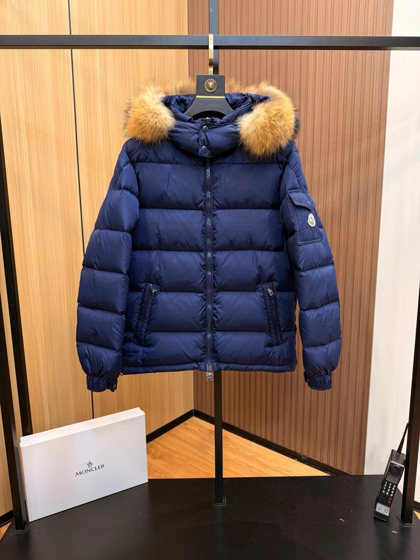 P1040 Moncler Mayaf short men's down jacket. The hood is removable. The fur collar is removable. Based on Maya, a removable fur collar is added. The Mayaf men's hooded down jacket is made of functional nylon fabric, and the hood is equipped with removable synthetic material trim.  The Mayaf short down jacket is a reinterpretation of the classic Moncler Maya style in an instantly recognizable silhouette, with a removable hood and adjustable hem. Made from functional fabric with removable synthetic trim on the hood. The sleeves are embellished with classic patch pockets, reflecting the brand's signature style. Details •Made from functional fabric •Technical fabric lining •Down-filled •Push-stud collar •Detachable hood with removable synthetic trim •Zip closure •Zip pockets •Patch pockets with press-stud •Adjustable elastic cuffs •Adjustable drawstring hem