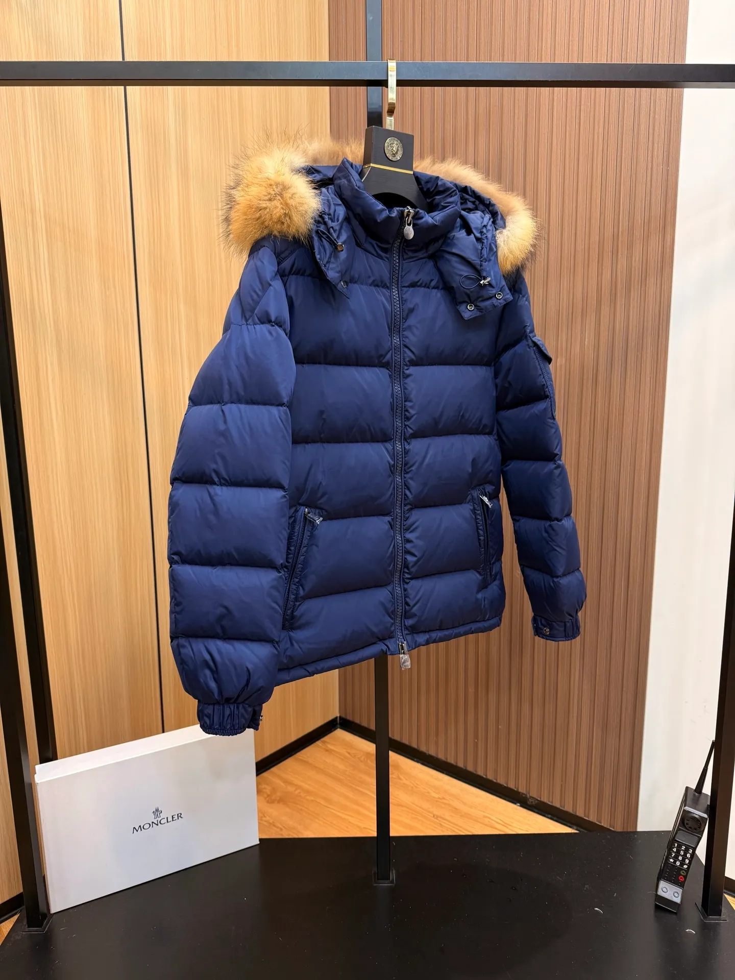 P1040 Moncler Mayaf short men's down jacket. The hood is removable. The fur collar is removable. Based on Maya, a removable fur collar is added. The Mayaf men's hooded down jacket is made of functional nylon fabric, and the hood is equipped with removable synthetic material trim.  The Mayaf short down jacket is a reinterpretation of the classic Moncler Maya style in an instantly recognizable silhouette, with a removable hood and adjustable hem. Made from functional fabric with removable synthetic trim on the hood. The sleeves are embellished with classic patch pockets, reflecting the brand's signature style. Details •Made from functional fabric •Technical fabric lining •Down-filled •Push-stud collar •Detachable hood with removable synthetic trim •Zip closure •Zip pockets •Patch pockets with press-stud •Adjustable elastic cuffs •Adjustable drawstring hem