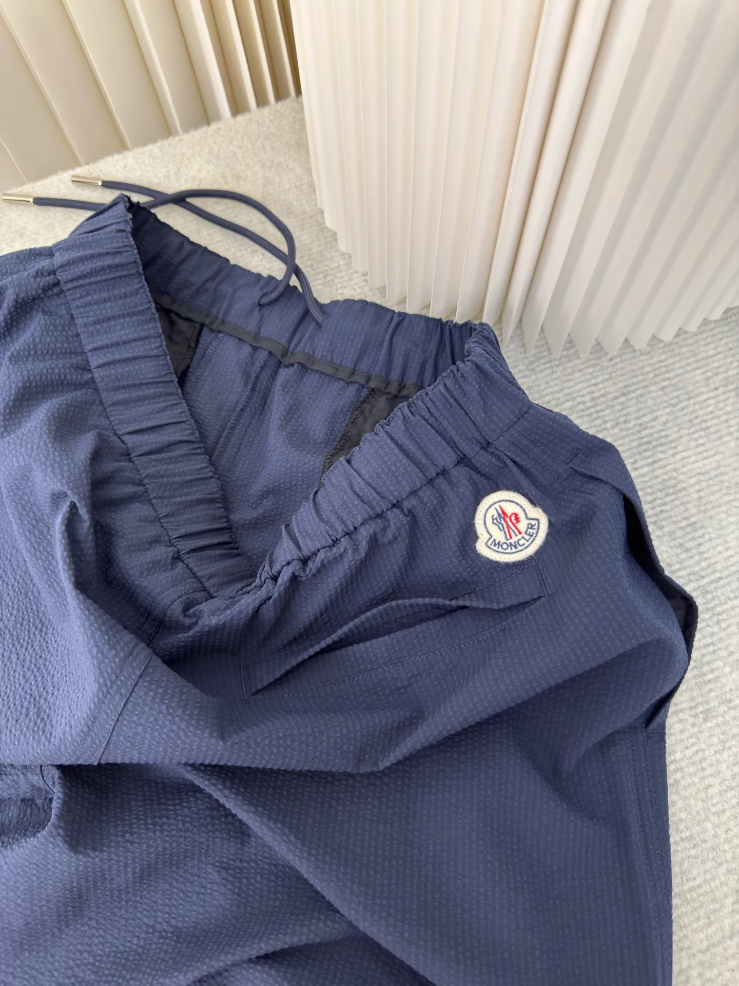 P310 MONCLER Puff Wrinkle Label Shorts with Mouth, Authentic Open Version - Physical Counter - Top Luxury Quality 🆚Second Price of All Versions on the Market Made of cotton blended woven fabric with 76% high cotton content + 24% polyester fiber. The high cotton content ensures that the fabric is soft, skin-friendly, and has good breathability. The addition of a small amount of polyester fiber balances the wrinkle resistance and elasticity of the overall fabric and greatly reduces its shrinkage. After preshrinking, dimensional changes during washing are negligible. The fusion of the two makes the fabric combine anti-wrinkle, quick-drying, easy care and other characteristics without losing the advantages of good wearing experience and strong breathability.  Bubble wrinkle technology: ground warp + bubble warp independent let-off. The bubble warp yarn feeding speed is about 20% higher than the ground warp yarn feeding speed. During weaving, the bubble warp is relaxed and accumulated, forming a naturally arched bubble unit. Through the alternating arrangement of yarns + floating length tissue changes, a clear grid frame is built between the bubble units, and finally the bubble three-dimensional effect and grid outline are locked through high-temperature heat setting. Size 1 2 3 4
