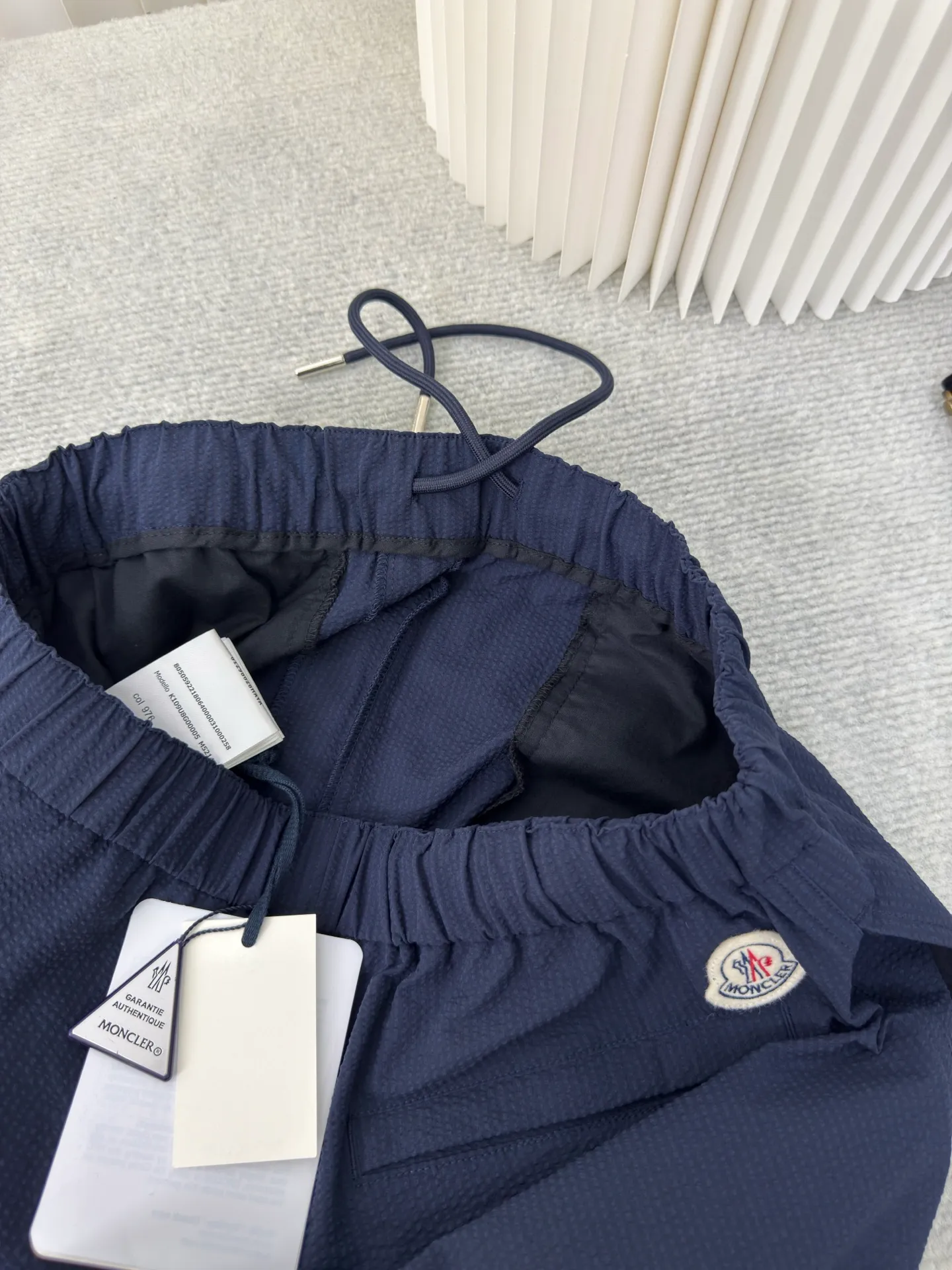 P310 MONCLER Puff Wrinkle Label Shorts with Mouth, Authentic Open Version - Physical Counter - Top Luxury Quality 🆚Second Price of All Versions on the Market Made of cotton blended woven fabric with 76% high cotton content + 24% polyester fiber. The high cotton content ensures that the fabric is soft, skin-friendly, and has good breathability. The addition of a small amount of polyester fiber balances the wrinkle resistance and elasticity of the overall fabric and greatly reduces its shrinkage. After preshrinking, dimensional changes during washing are negligible. The fusion of the two makes the fabric combine anti-wrinkle, quick-drying, easy care and other characteristics without losing the advantages of good wearing experience and strong breathability.  Bubble wrinkle technology: ground warp + bubble warp independent let-off. The bubble warp yarn feeding speed is about 20% higher than the ground warp yarn feeding speed. During weaving, the bubble warp is relaxed and accumulated, forming a naturally arched bubble unit. Through the alternating arrangement of yarns + floating length tissue changes, a clear grid frame is built between the bubble units, and finally the bubble three-dimensional effect and grid outline are locked through high-temperature heat setting. Size 1 2 3 4
